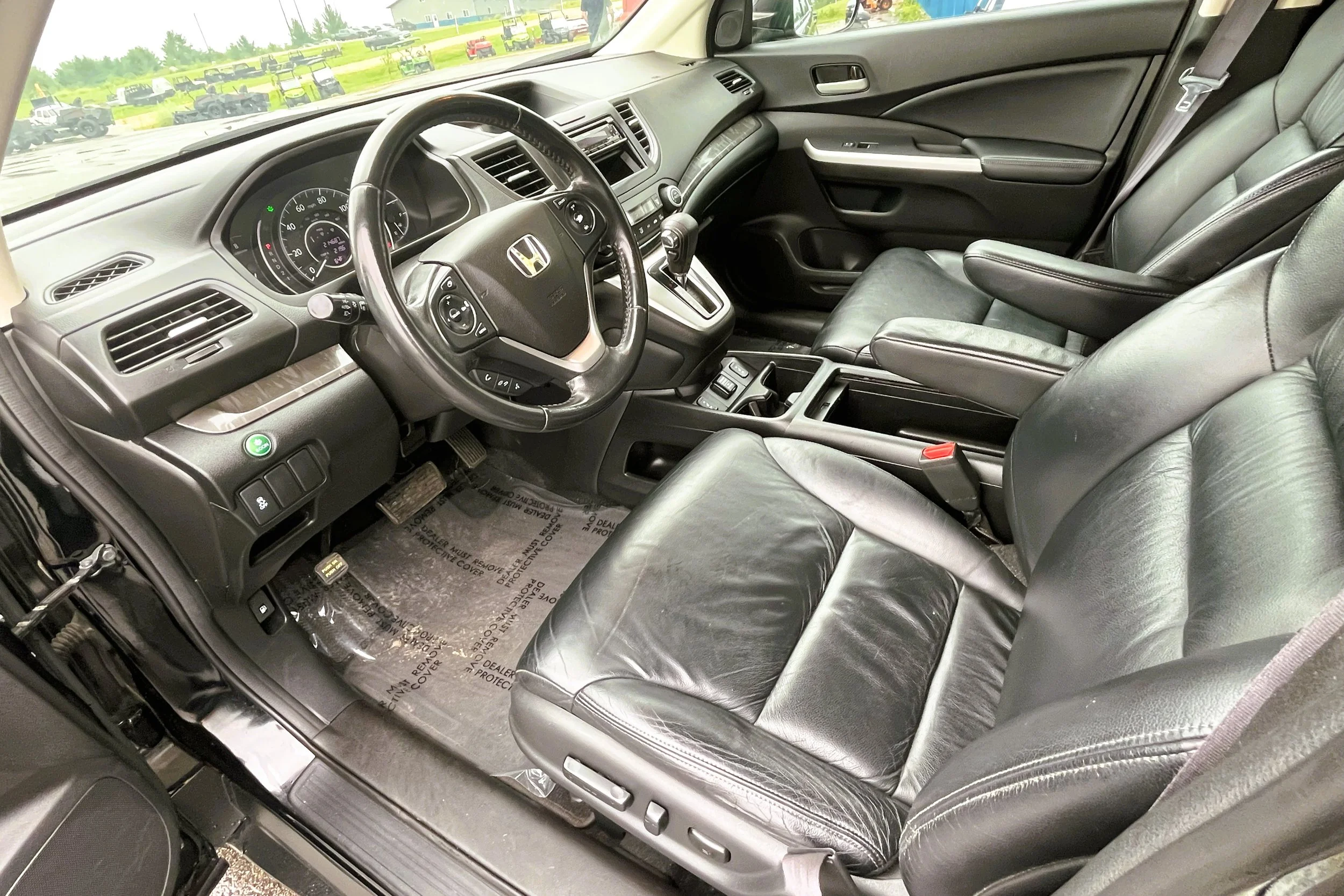 Interior of a black Honda vehicle showing the driver's seat, steering wheel, dashboard, and part of the front passenger seat with a view of a parking lot outside.