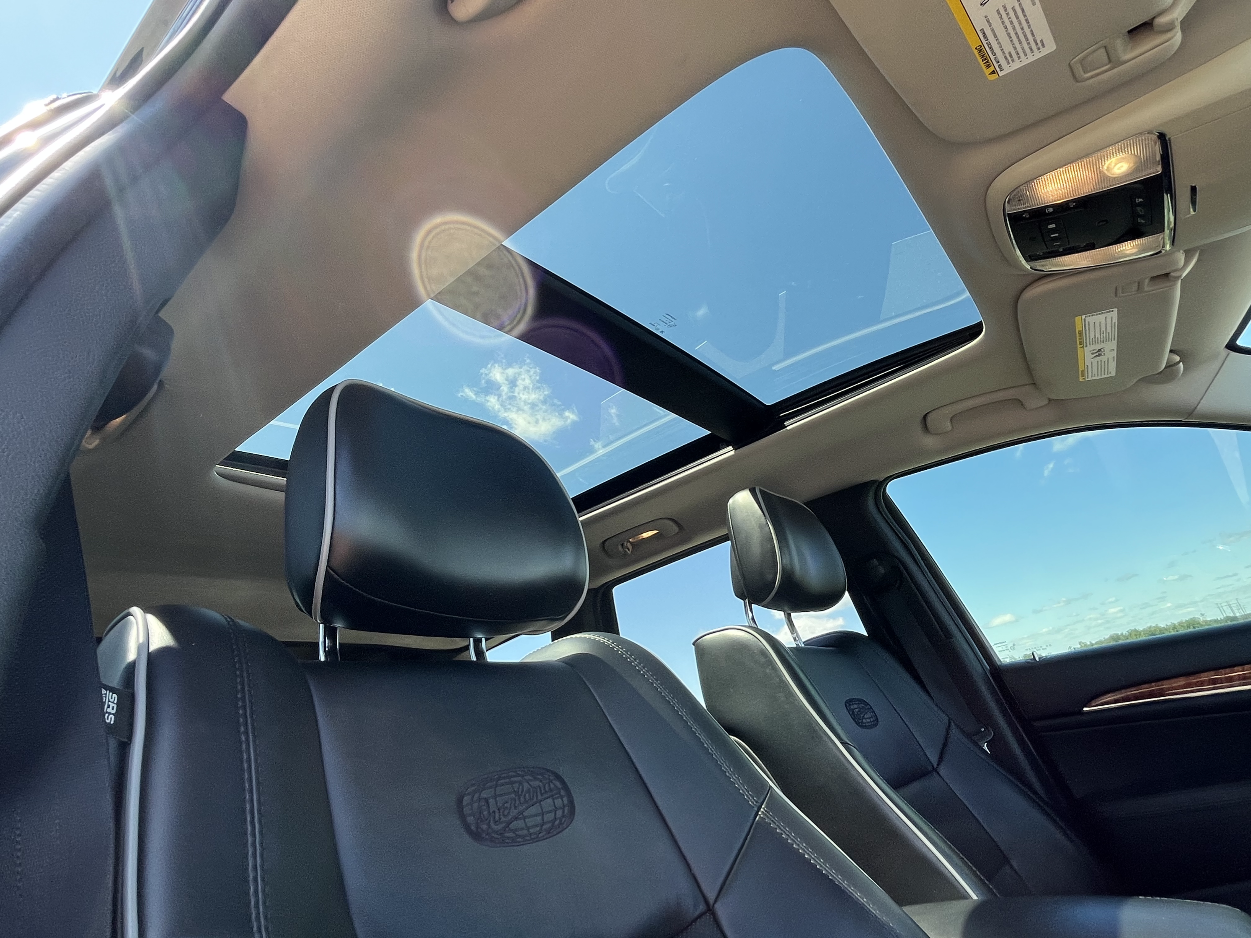 Inside view of a car with black leather seats and a panoramic sunroof showing a blue sky with some clouds.