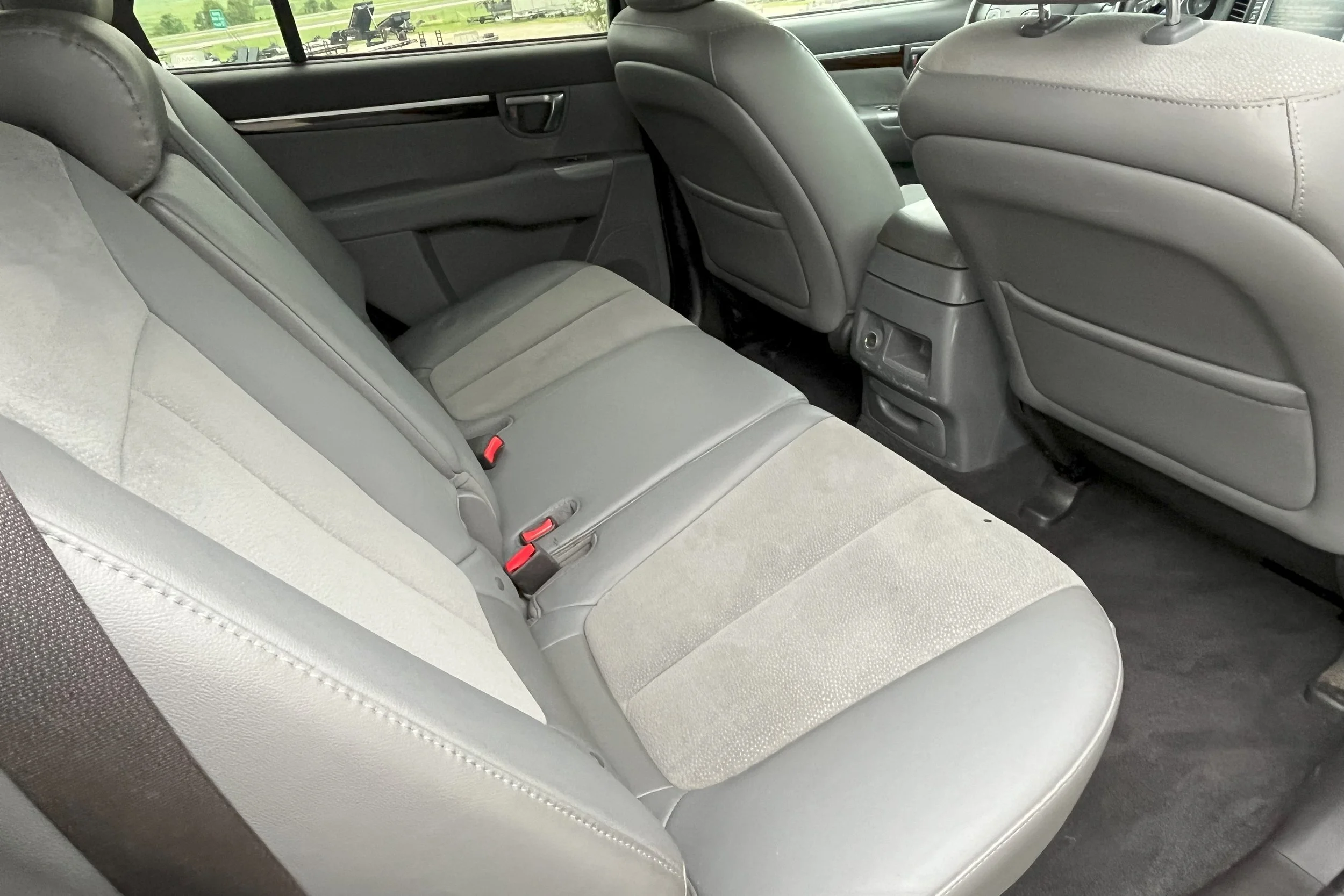 The interior of a car showing the backseat and front seats, upholstered in light gray fabric, with a view through the window of a green rural landscape.
