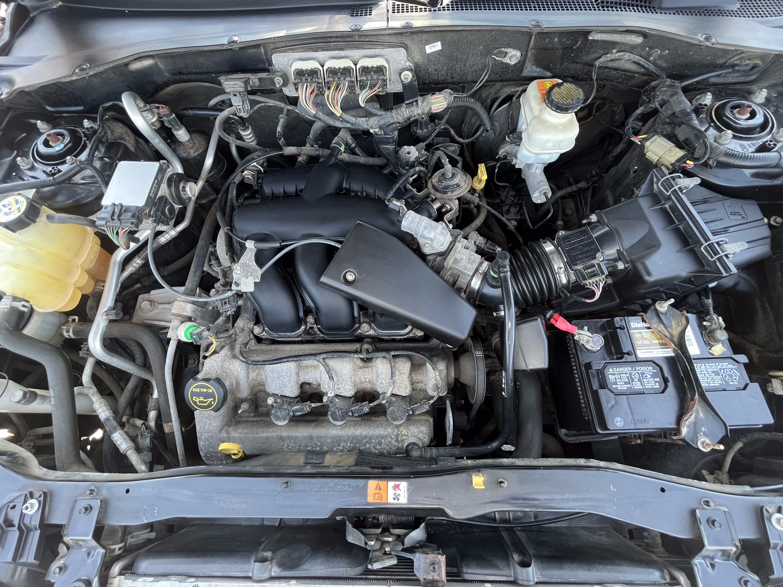 Car engine bay with various components including battery, air intake, coolant reservoir, and engine parts.