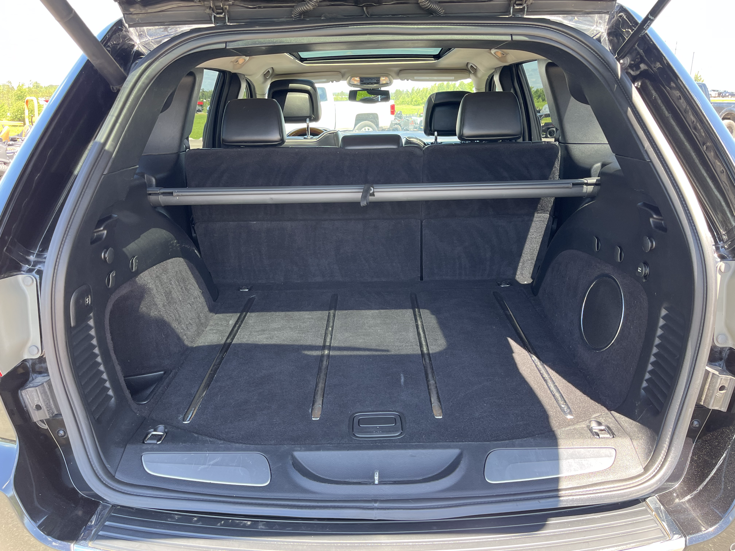Empty car trunk with a protective cover bar, black interior, and rear seats visible, parked outdoors on a sunny day.