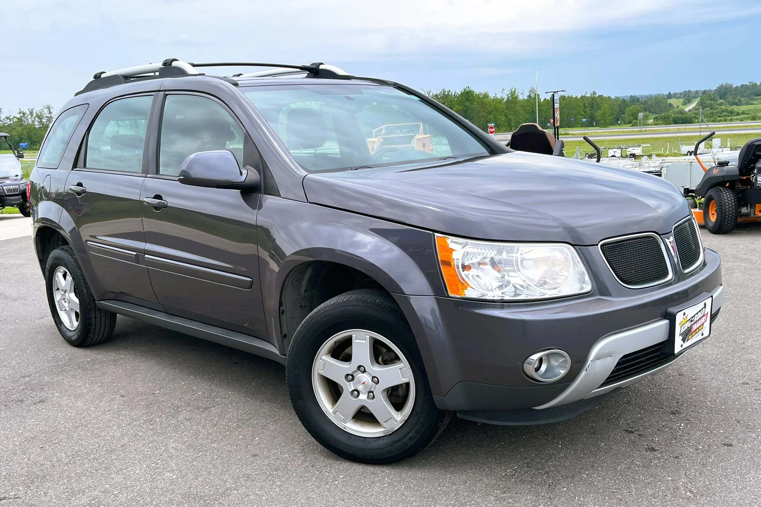 Gray SUV parked outdoors on a gray asphalt lot with trees and a grassy hill in the background.