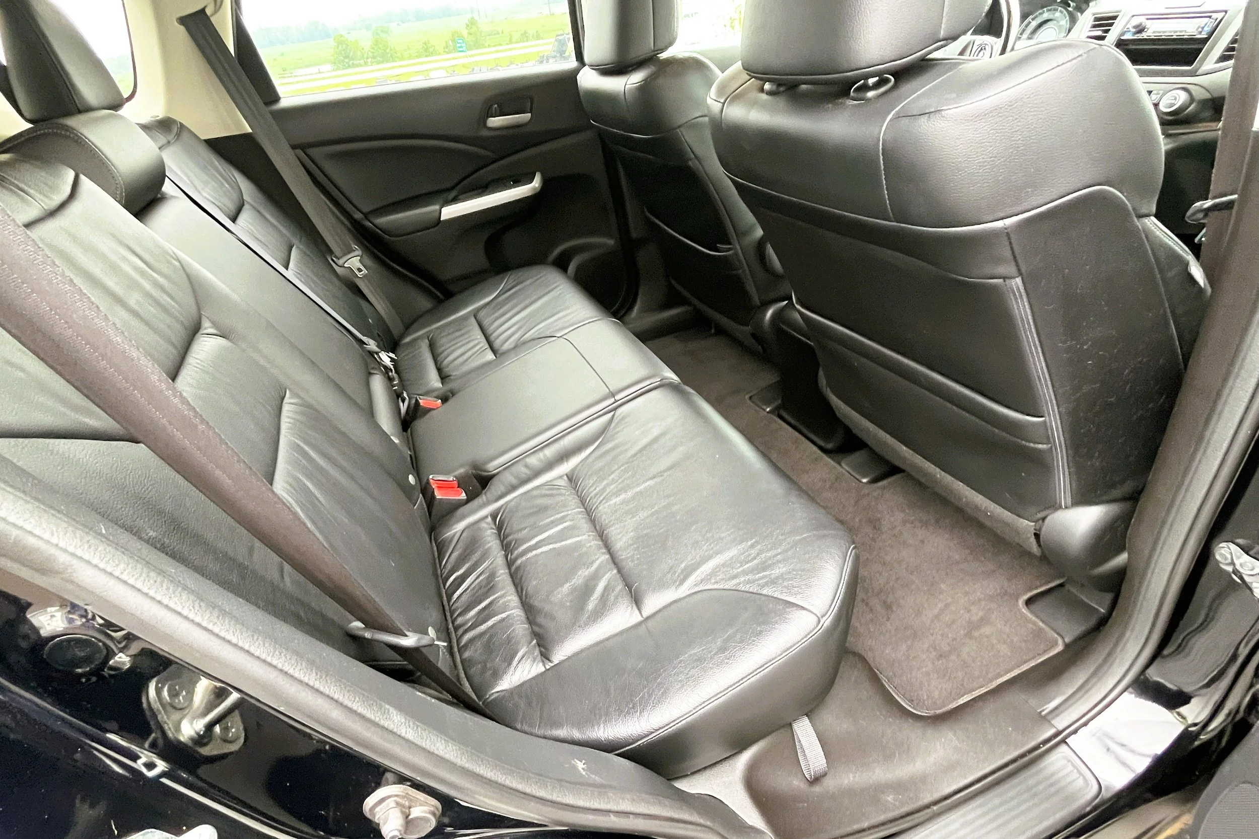 Interior of a black vehicle showing the back and front seats, all in black leather, with the rear seats having three seat belts, and the car door and window visible.