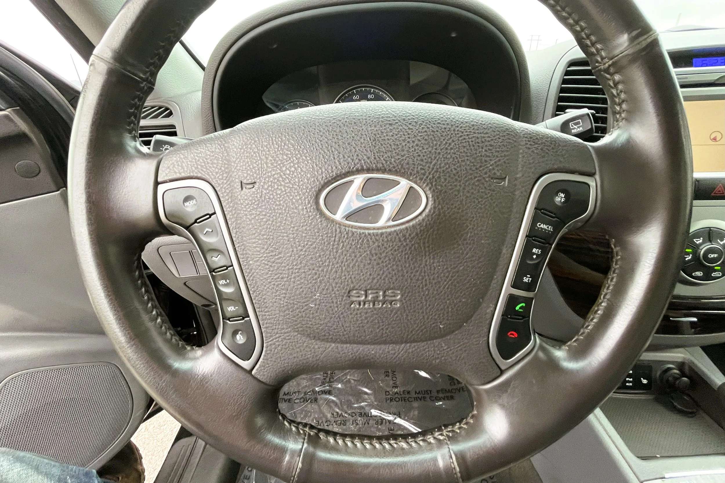 Close-up of a Hyundai car steering wheel with buttons for audio and cruise control, and the Hyundai logo in the center.