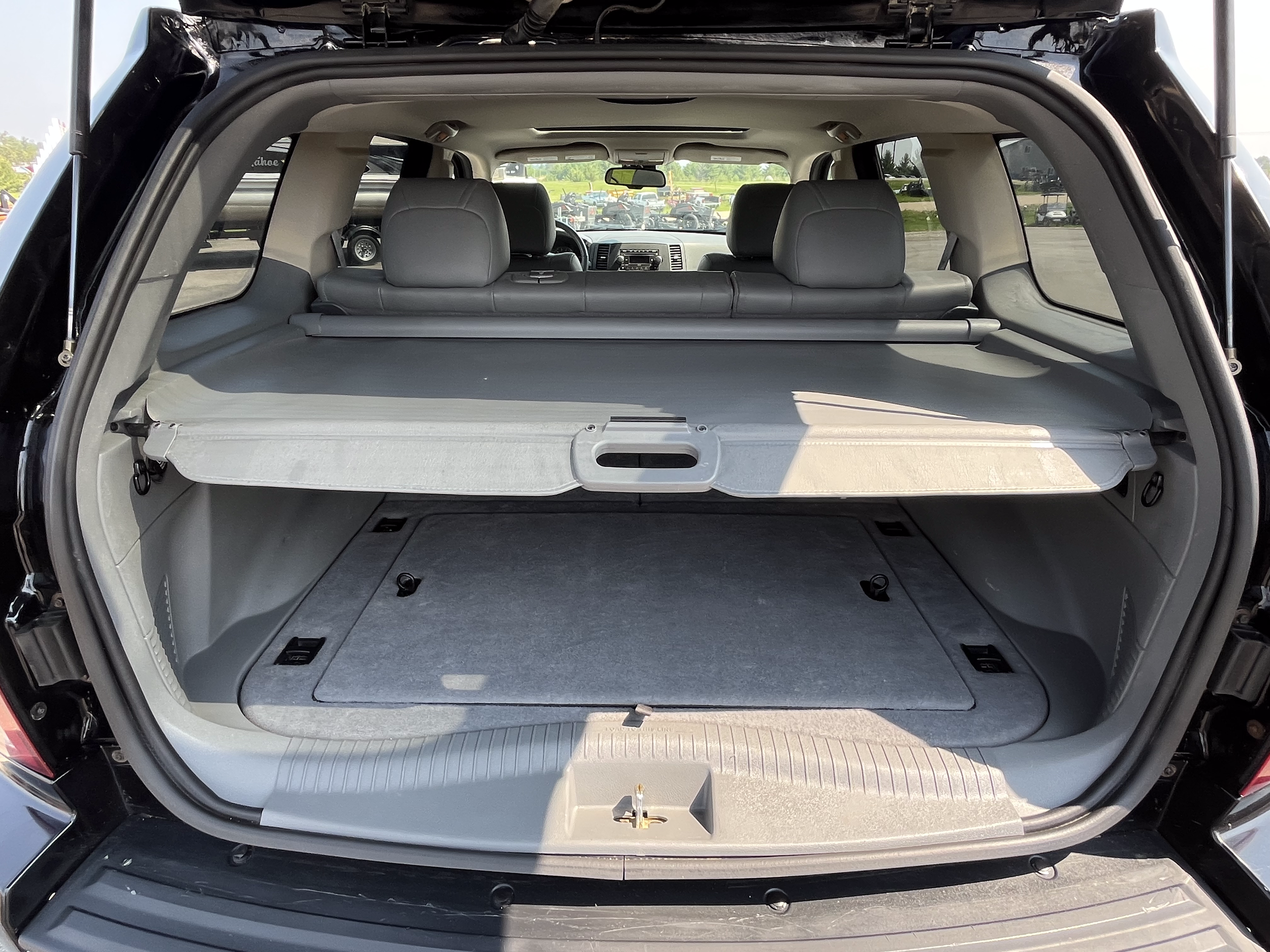 Open trunk of a black SUV showing a large cargo area with a retractable cover, gray interior lining, and multiple anchor points, with the back seats and vehicle's dashboard visible in the background.