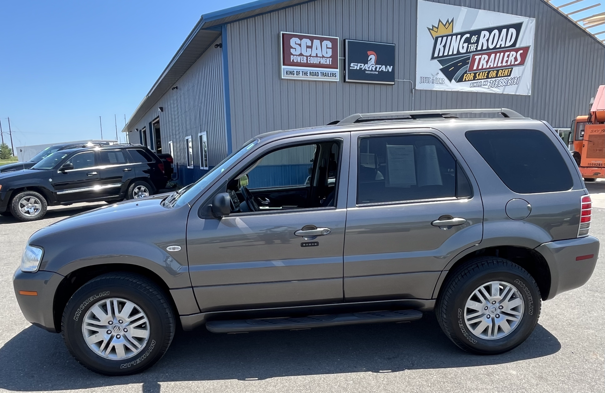 Gray SUV parked in front of a dealership with signs for trailers and power equipment.