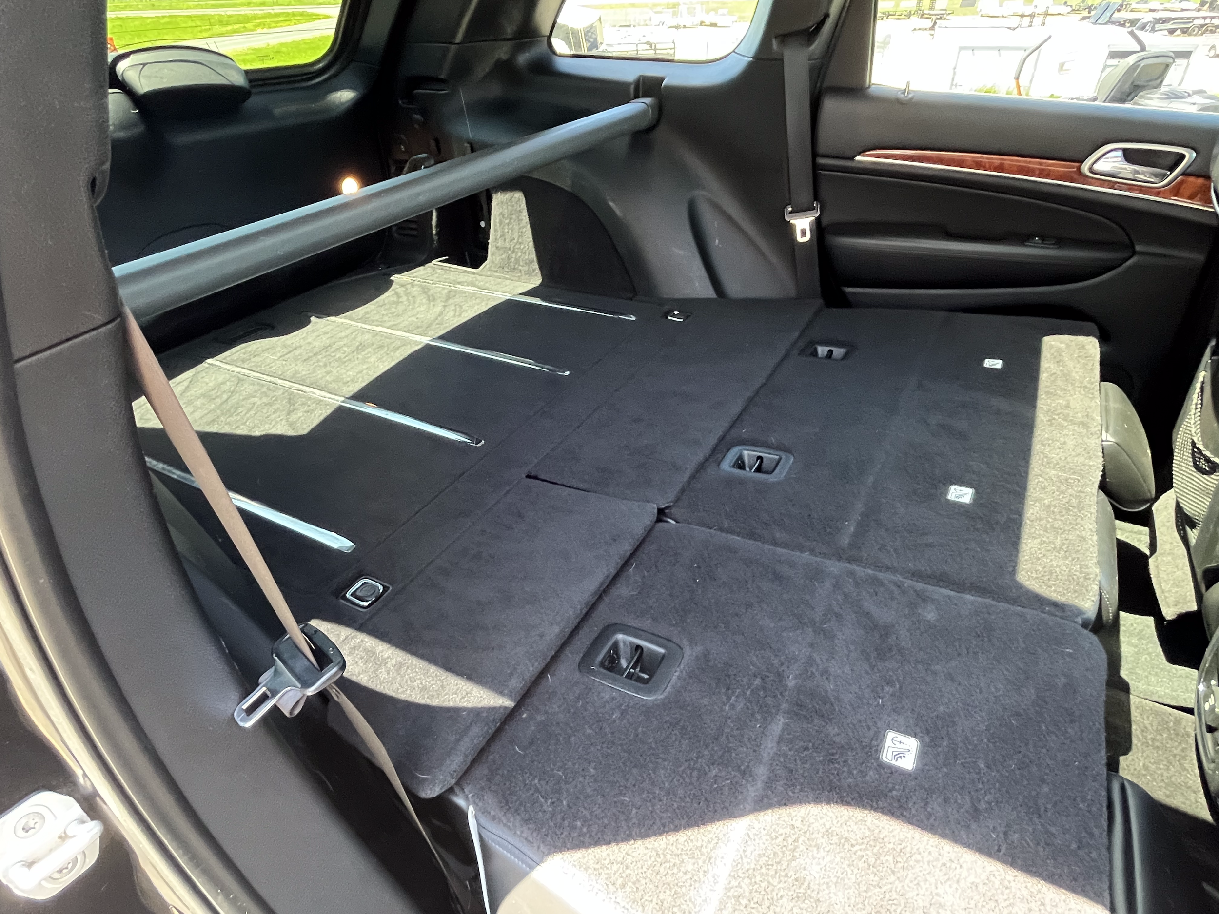 Back of a vehicle with folded down rear seats, showing a spacious cargo area with a grab bar, interior carpeting, and seat anchors.