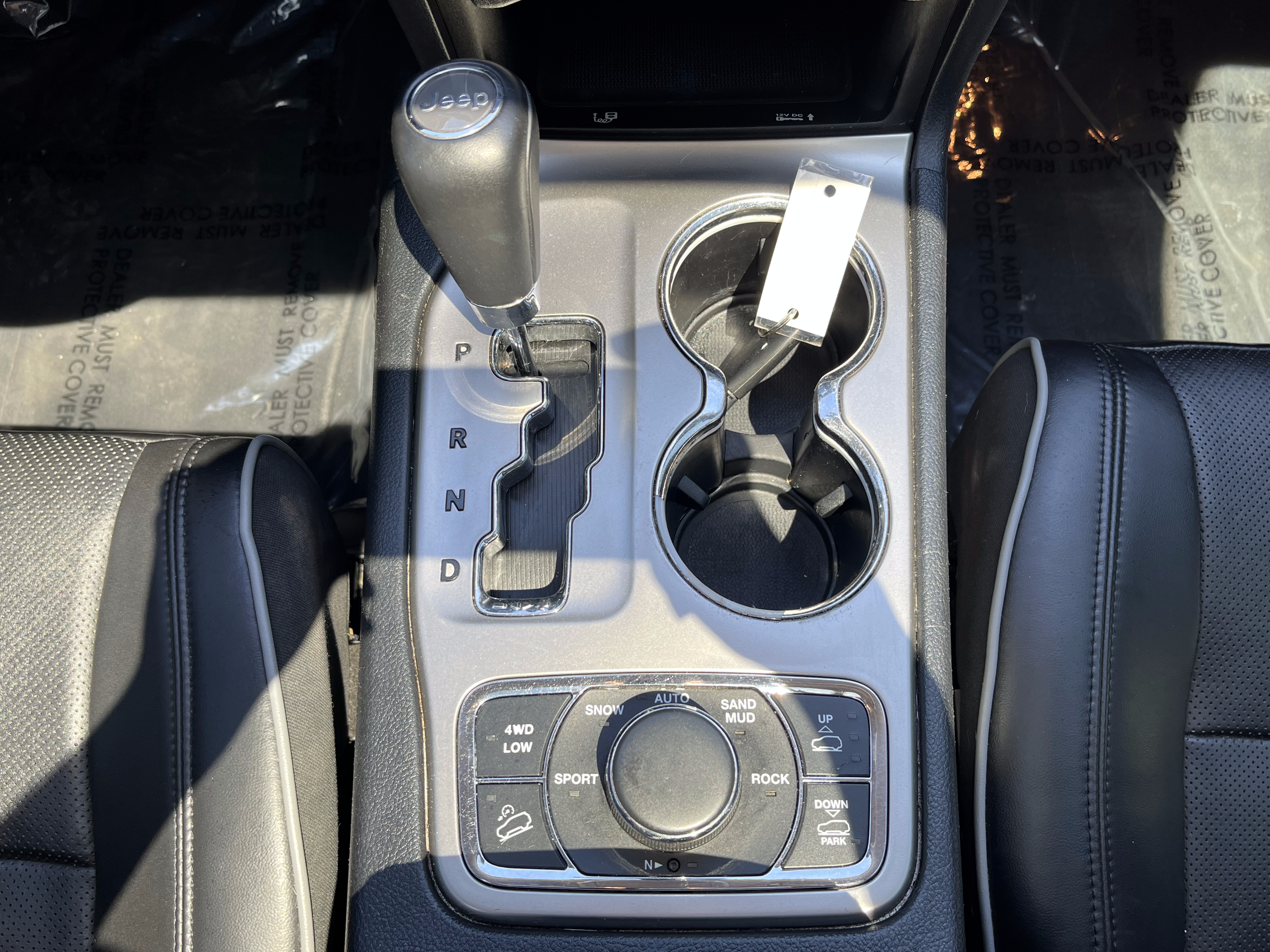 Center console of a Jeep vehicle showing an automatic gear shift, cup holders, and a control dial for off-road modes.