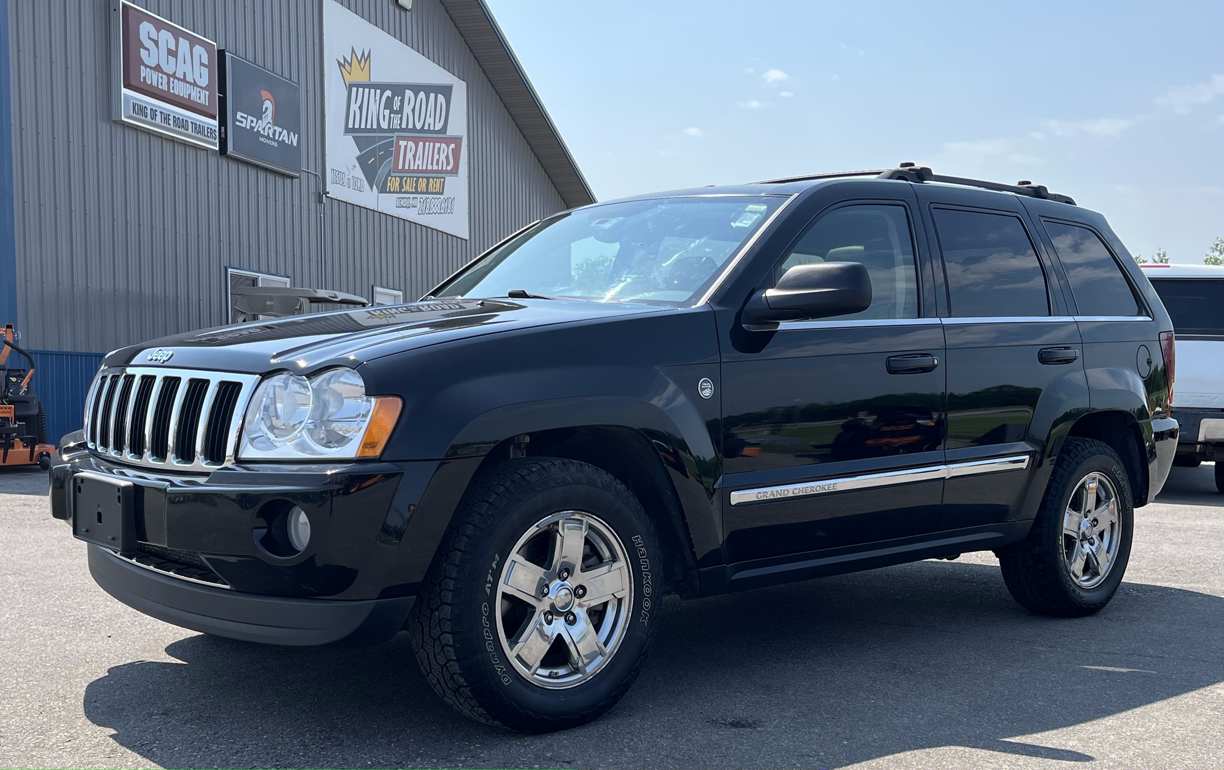 A black Jeep Grand Cherokee parked in front of a building with signs for trailers and power equipment.