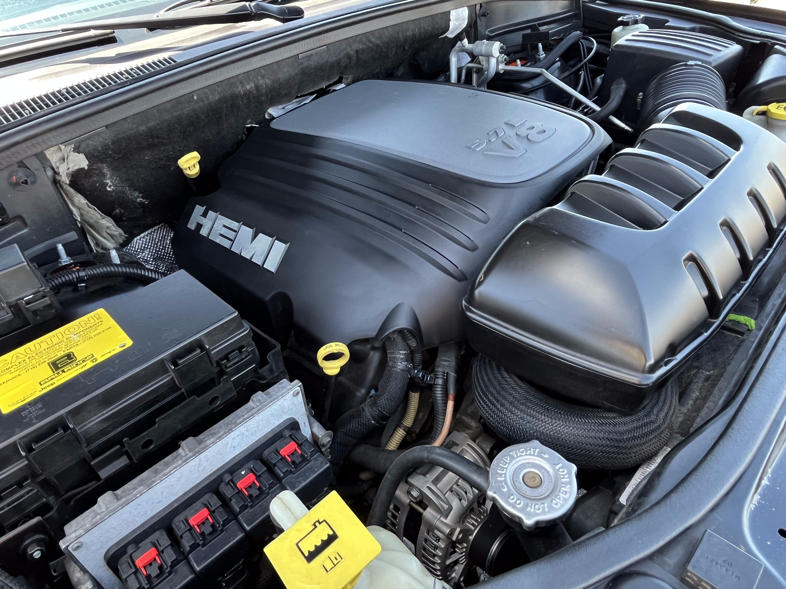 Car engine bay with a HEMI engine cover and various engine components visible.