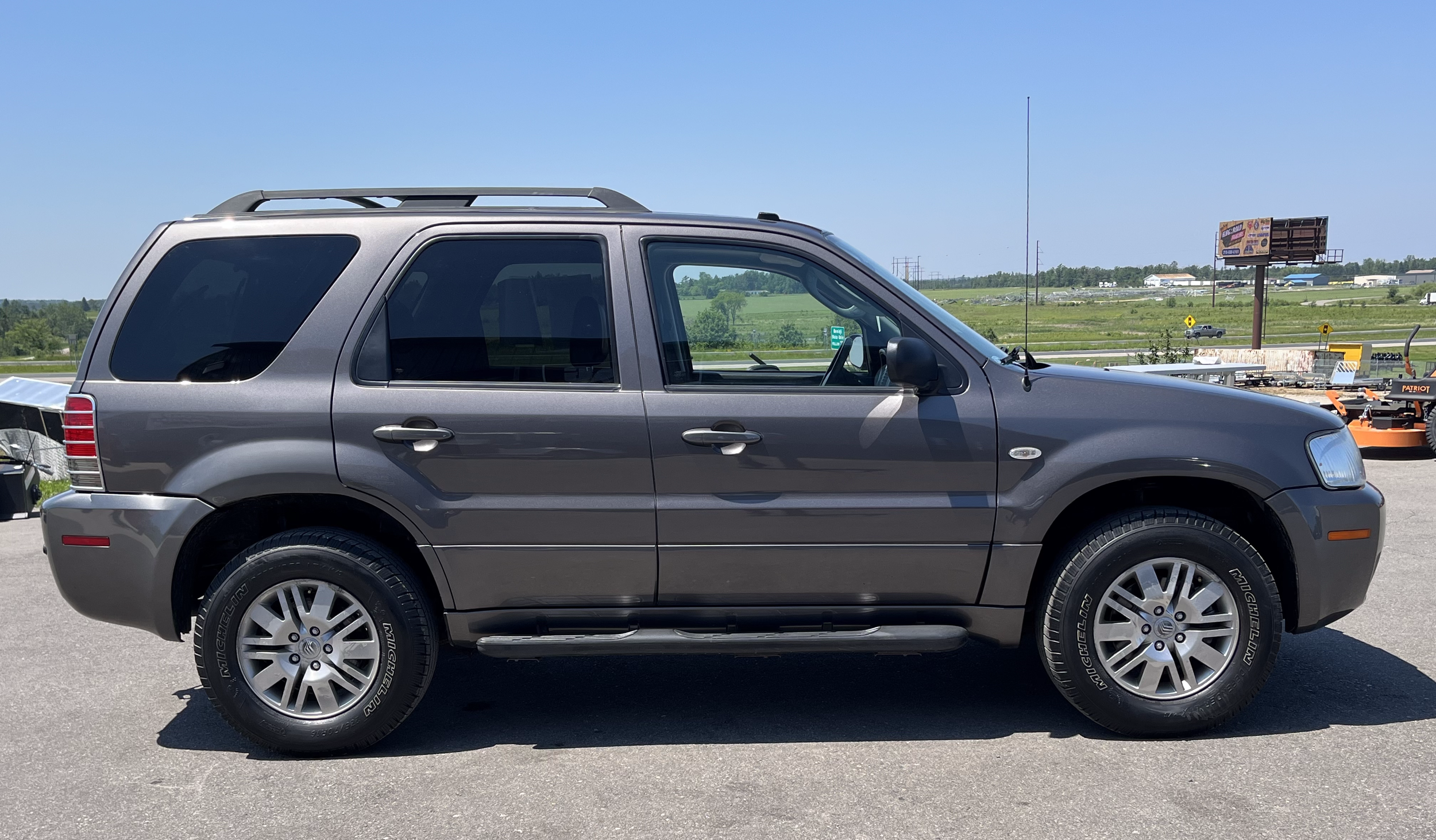 Gray SUV parked in a lot with a grassy landscape and blue sky in the background.