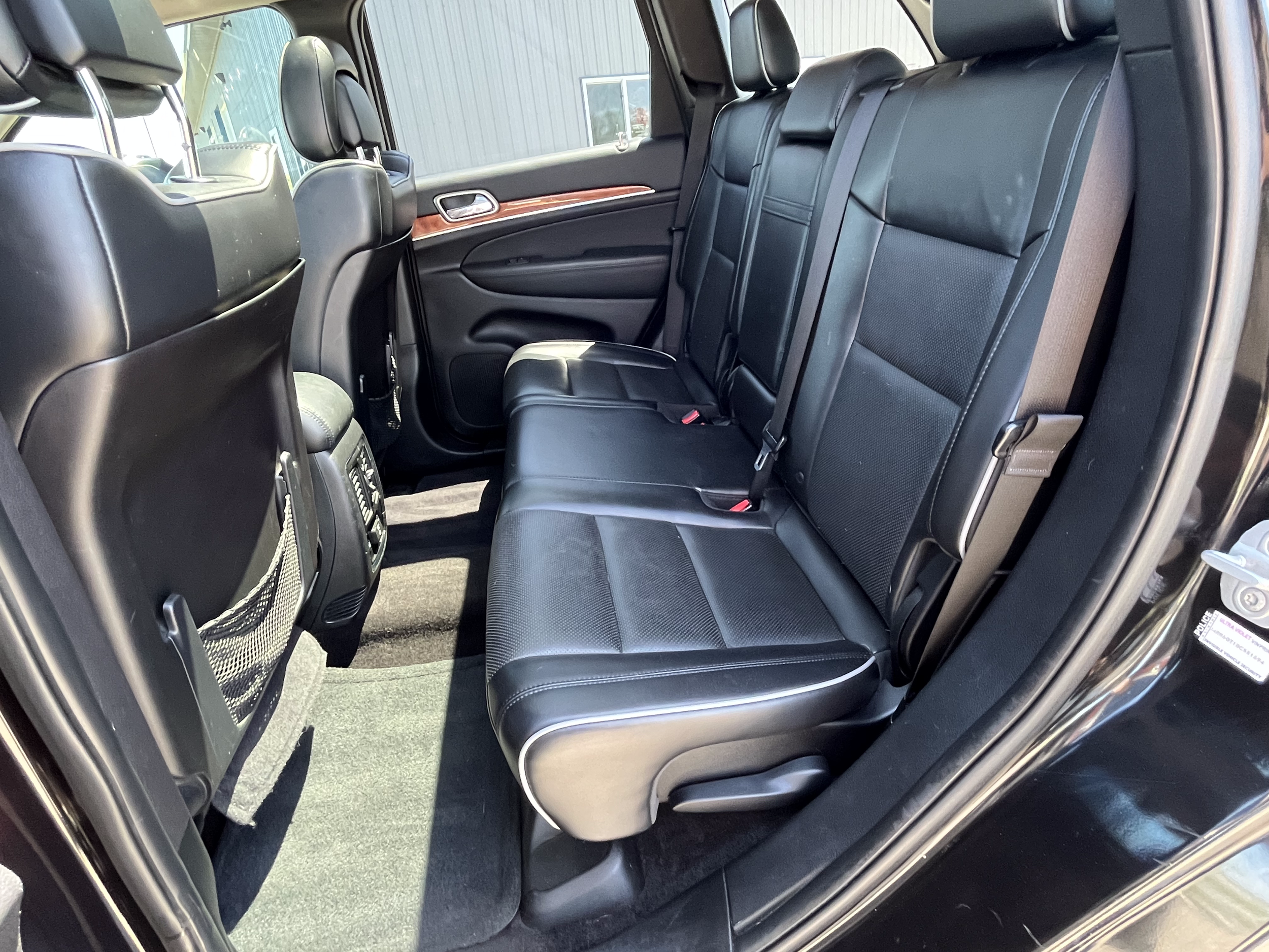 The rear interior of a vehicle showing black leather seats, headrests, seat belts, seat pockets on the back of the front seats, and a center console with climate controls.