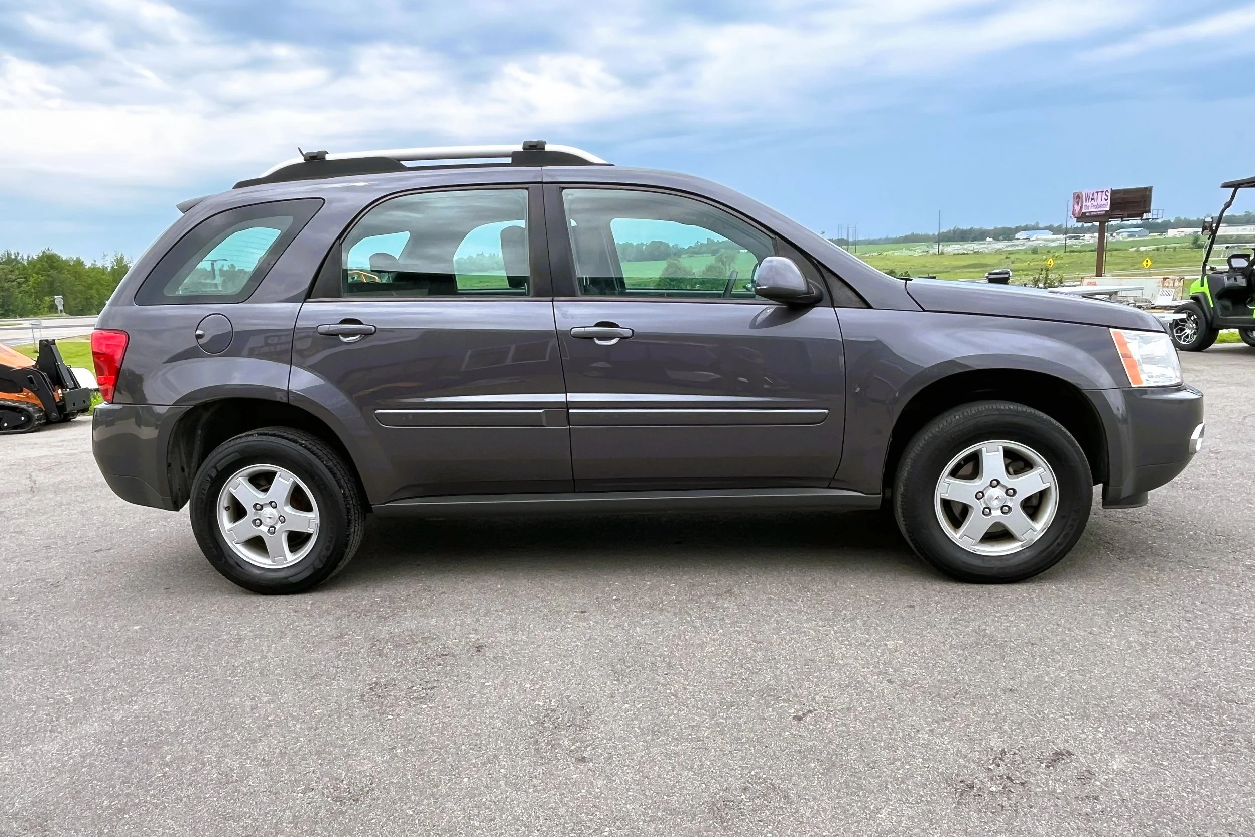 Gray Chrysler Pacifica SUV parked on a paved lot with a cloudy sky in the background.