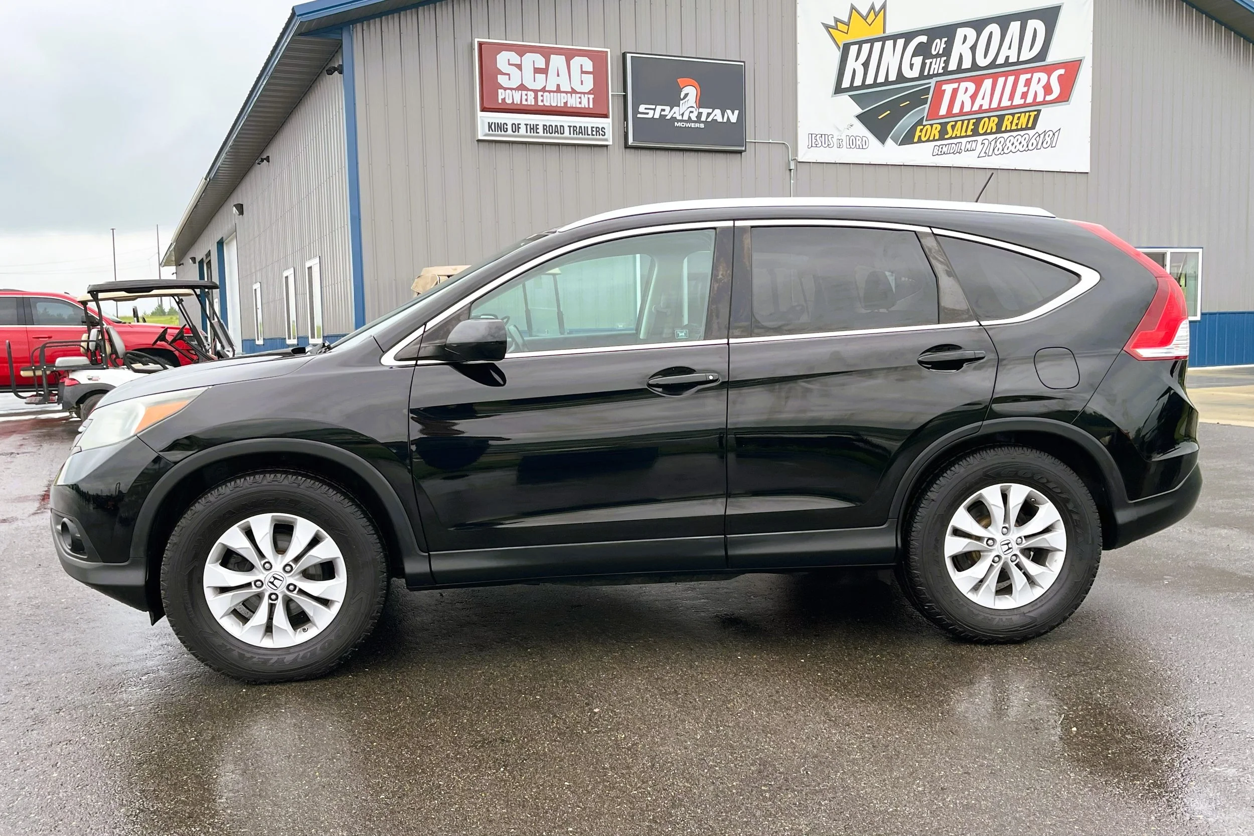 Black Honda SUV parked outside a dealership with a large sign. The dealership has signs for King of the Road Trailers, Spartans Mowers, and SCAG Power Equipment.