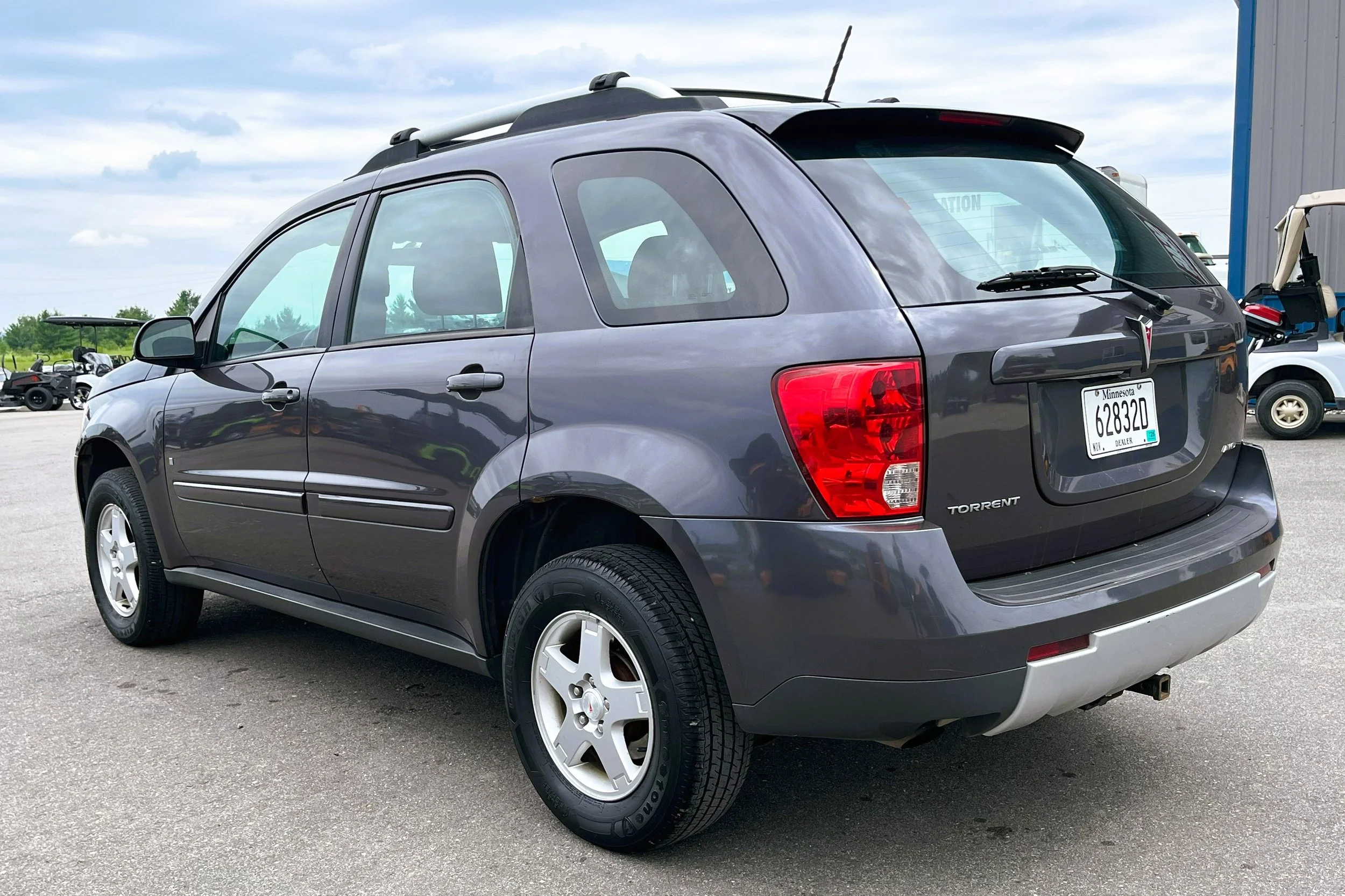Gray Pontiac Torrent SUV parked outdoors with a Minnesota license plate, in a lot with other vehicles and a building in the background.