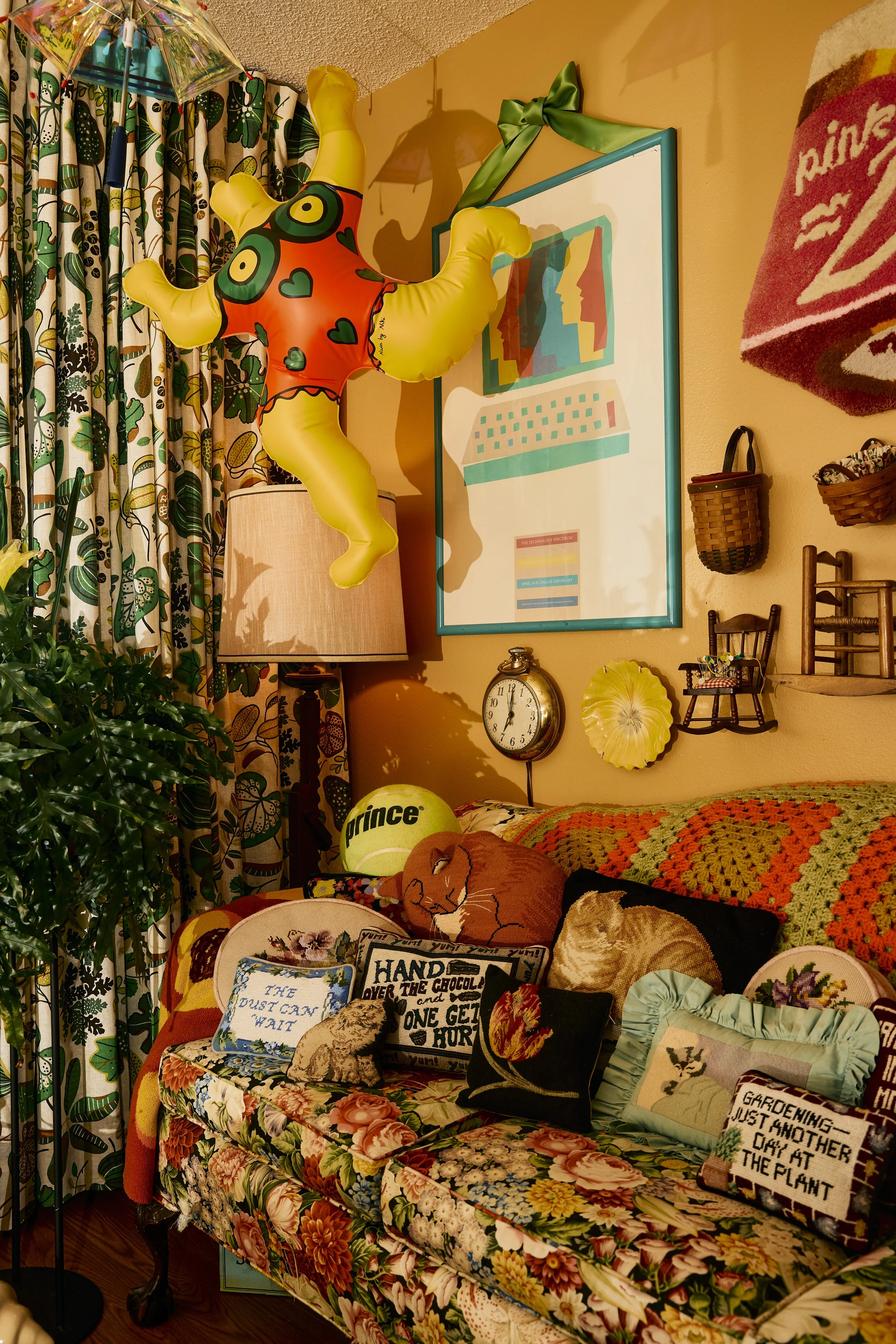 Floral couch with crocheted blanket and needlepoint pillows plus a blow-up doll make up a sitting room in Zach and Taylor's Houston, TX apartment. Image by Austin-based lifestyle photographer, Mackenzie Smith.