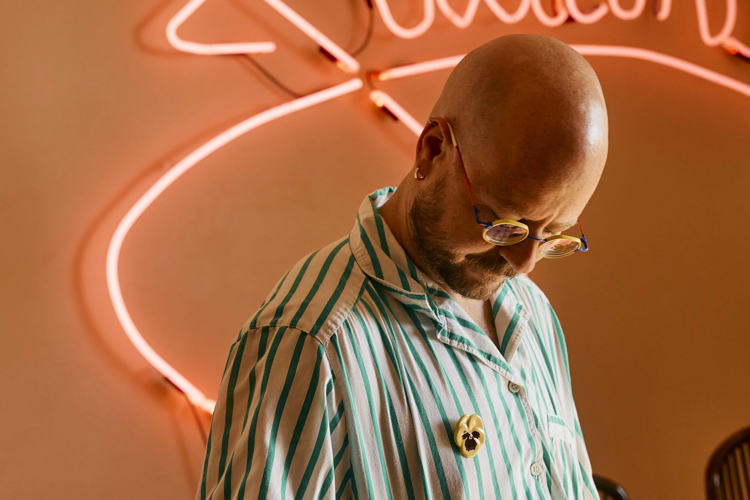 Portrait of Zach and his eclectic shirt pin in front of a pink neon sign in his dining room, Houston, TX. Image by Austin-based portrait photographer, Mackenzie Smith.