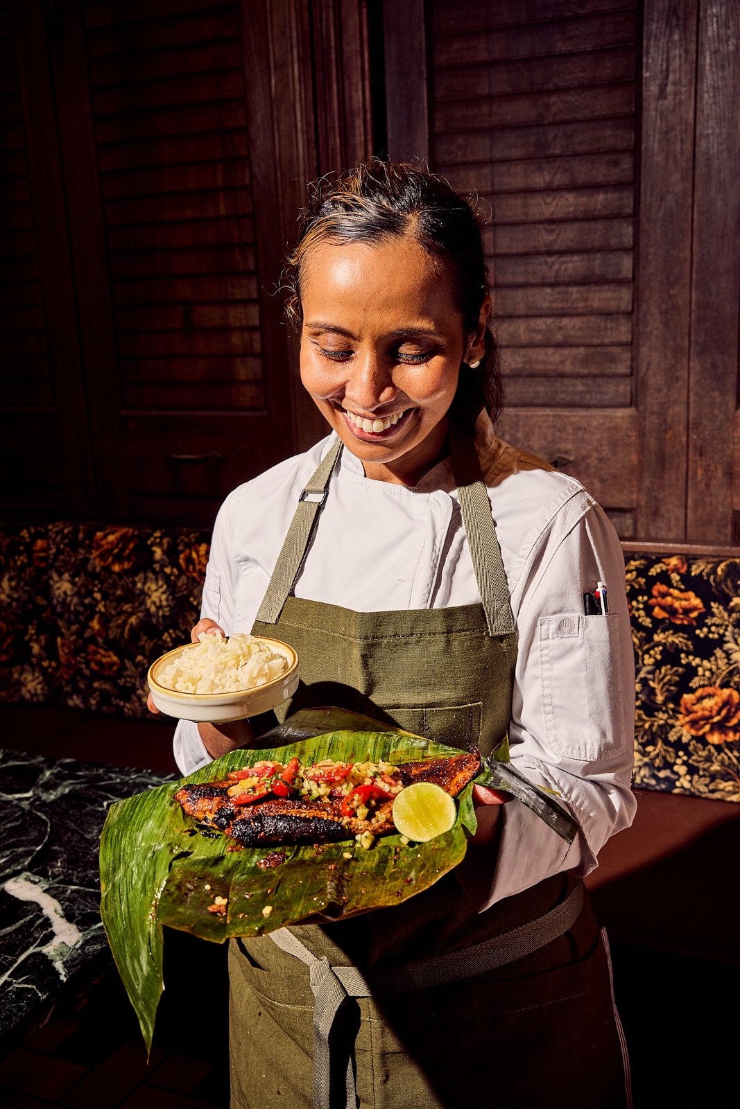 Chef Laila Bazahm holding the Sambal Striped Bass and rice, both cooked in banana leaf. Image by Austin-based portrait and food photographer, Mackenzie Smith.