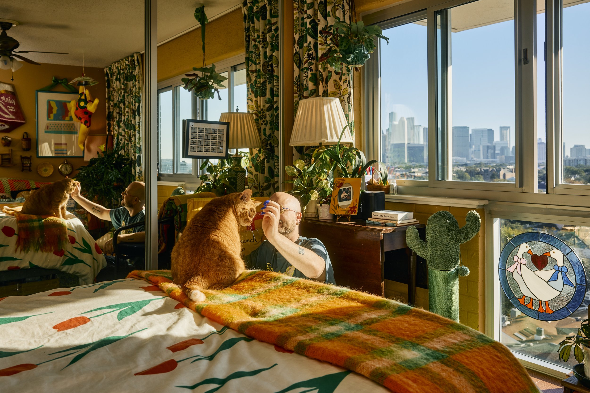 Zach and Stu the cat in their apartment bedroom with the Houston skyline view. Image by Austin-based lifestyle photographer, Mackenzie Smith.