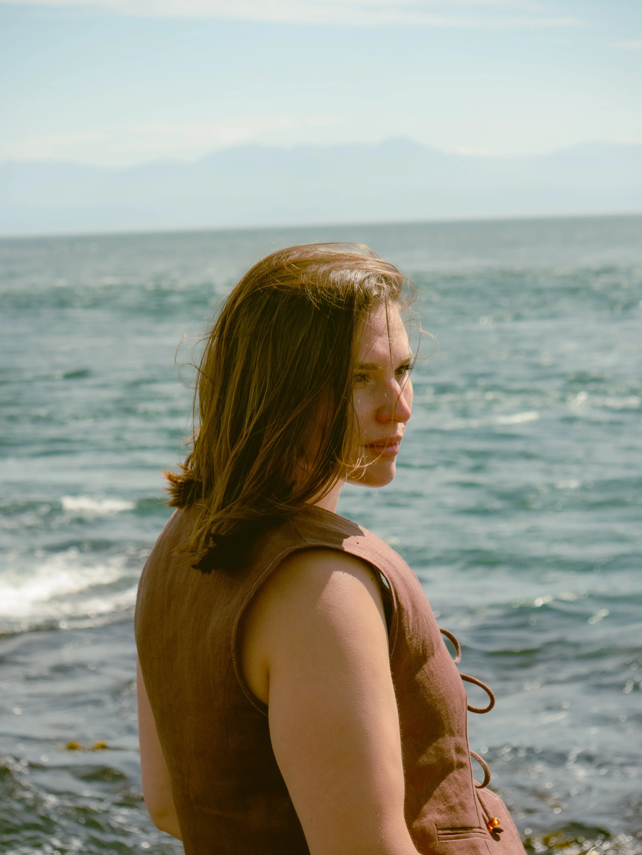 Lucy Randle standing by the ocean on a sunny day, with mountains in the background.