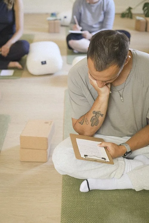 A man sitting on the floor holding a clipboard with his hand on his chin, pondering