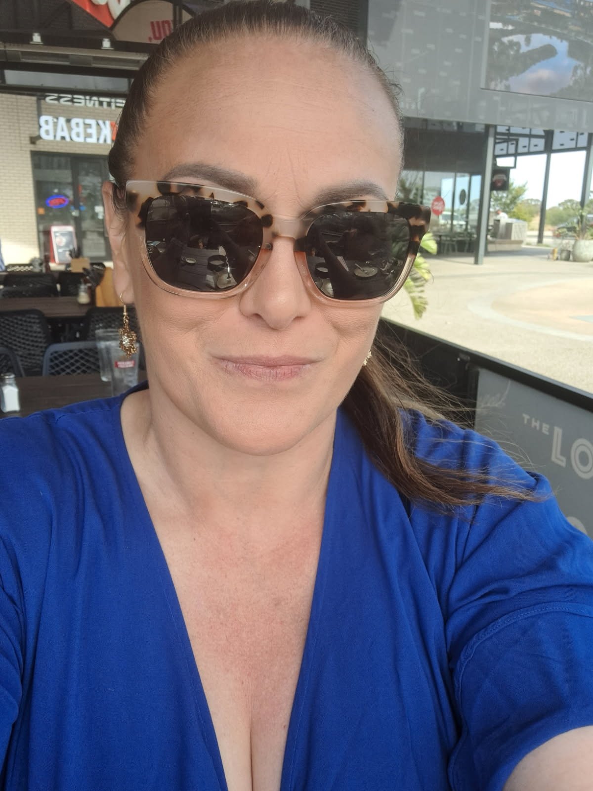A woman wearing sunglasses and a blue top taking a selfie inside a restaurant.