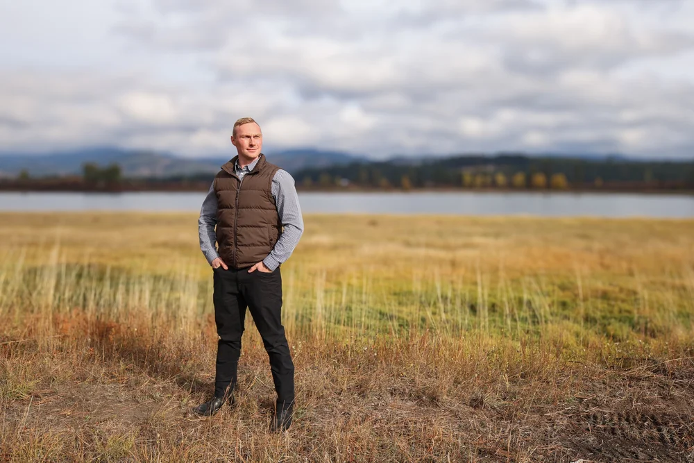 Jacob Mack standing in an open field with a lake and mountains in the background