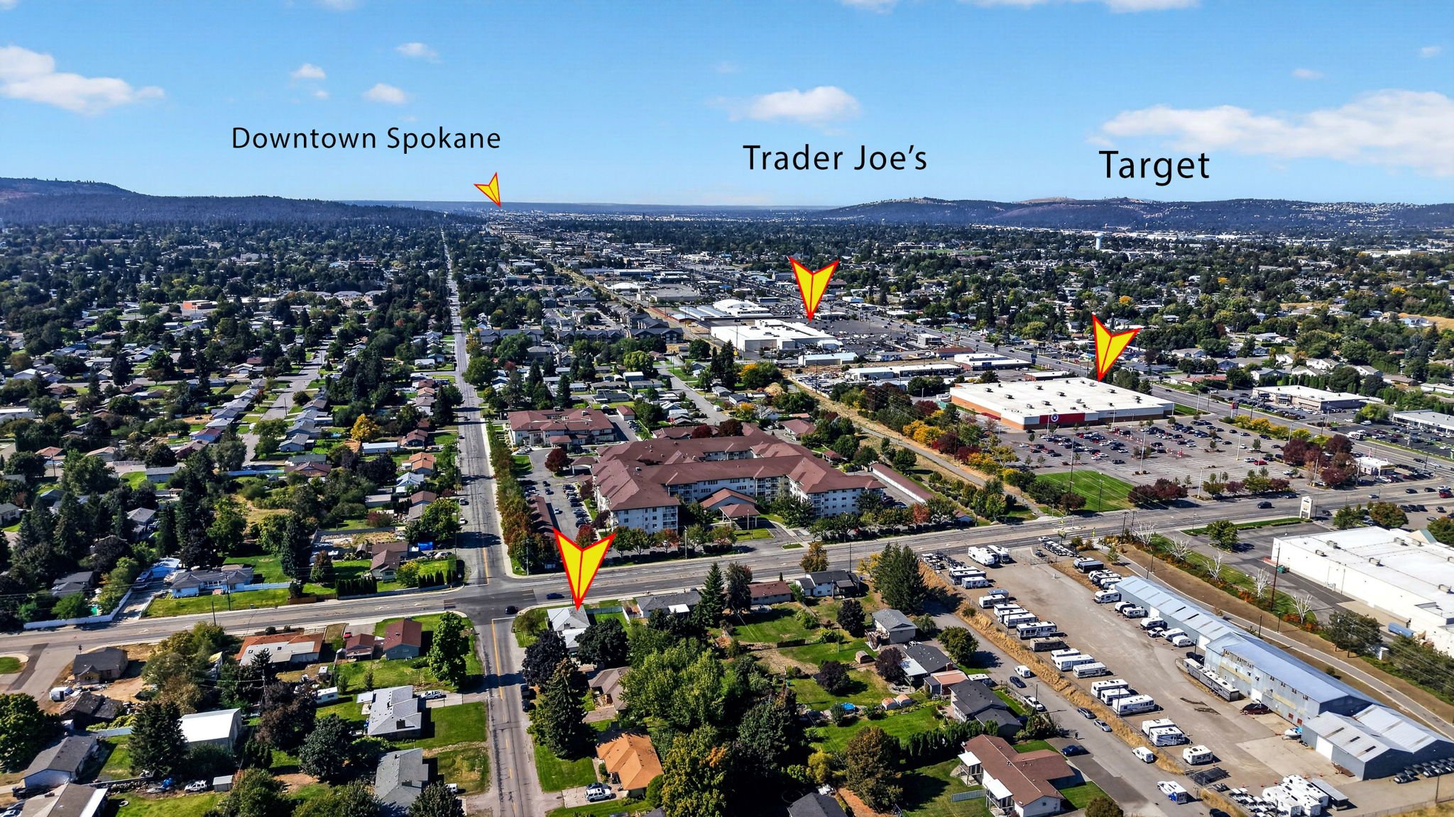 Aerial view of a residential and commercial area in Spokane, showing neighborhoods, shopping centers, parking lots, and distant hills with labeled locations: Downtown Spokane, Trader Joe's, and Target.