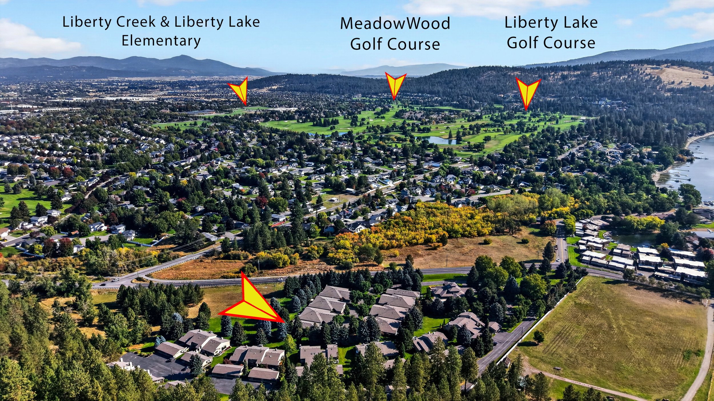 Aerial view of a suburban neighborhood with houses surrounded by trees, a river on the right, and mountains in the background. There are labels pointing to Liberty Creek & Liberty Lake Elementary, MeadowWood Golf Course, and Liberty Lake Golf Course,