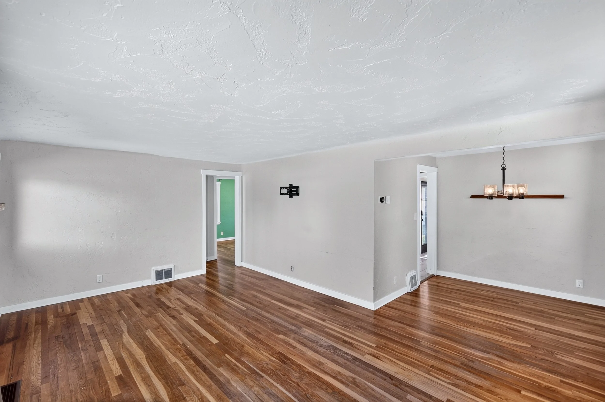 Empty living room with white walls, wooden floor, and a modern hanging light fixture.