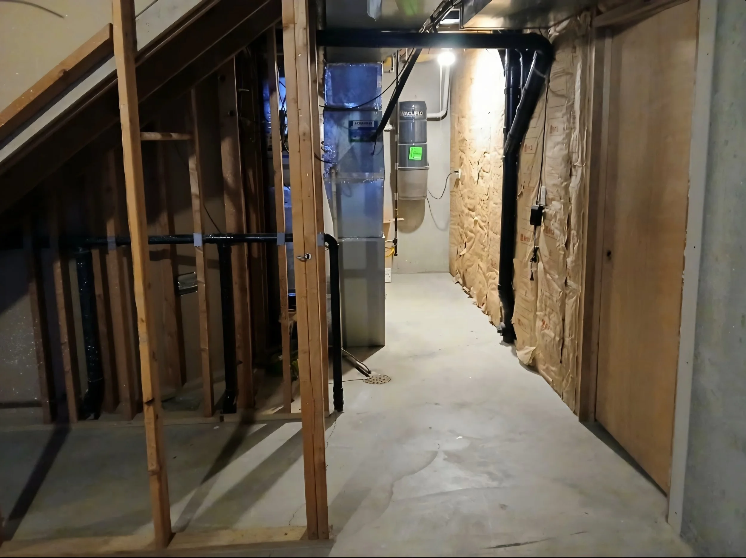 This is a construction site or basement with wooden framing and plumbing pipes visible, with an HVAC unit in the background.