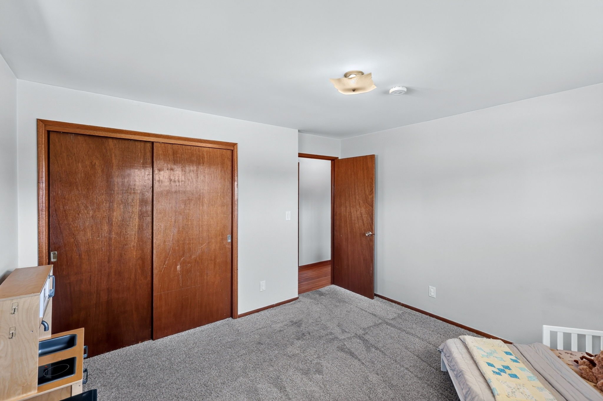 Empty bedroom with a closet, a bed with a teddy bear, and a small wooden toy kitchen set.