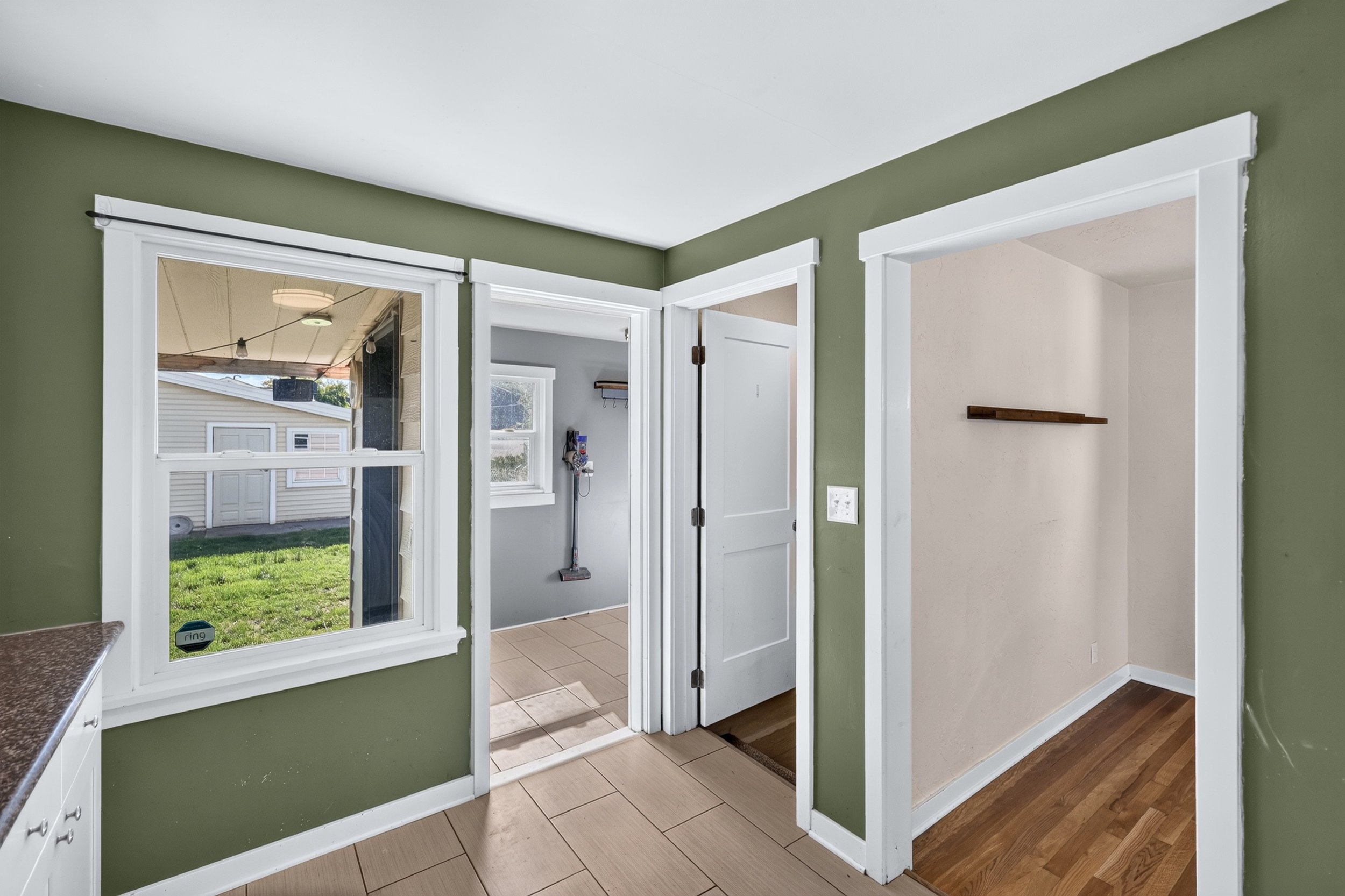 Interior view of a room with green walls, white trim, and a doorway leading to a small tiled area with a white door and window, and a backyard outside. Part of a countertop with a speckled surface is visible on the left.
