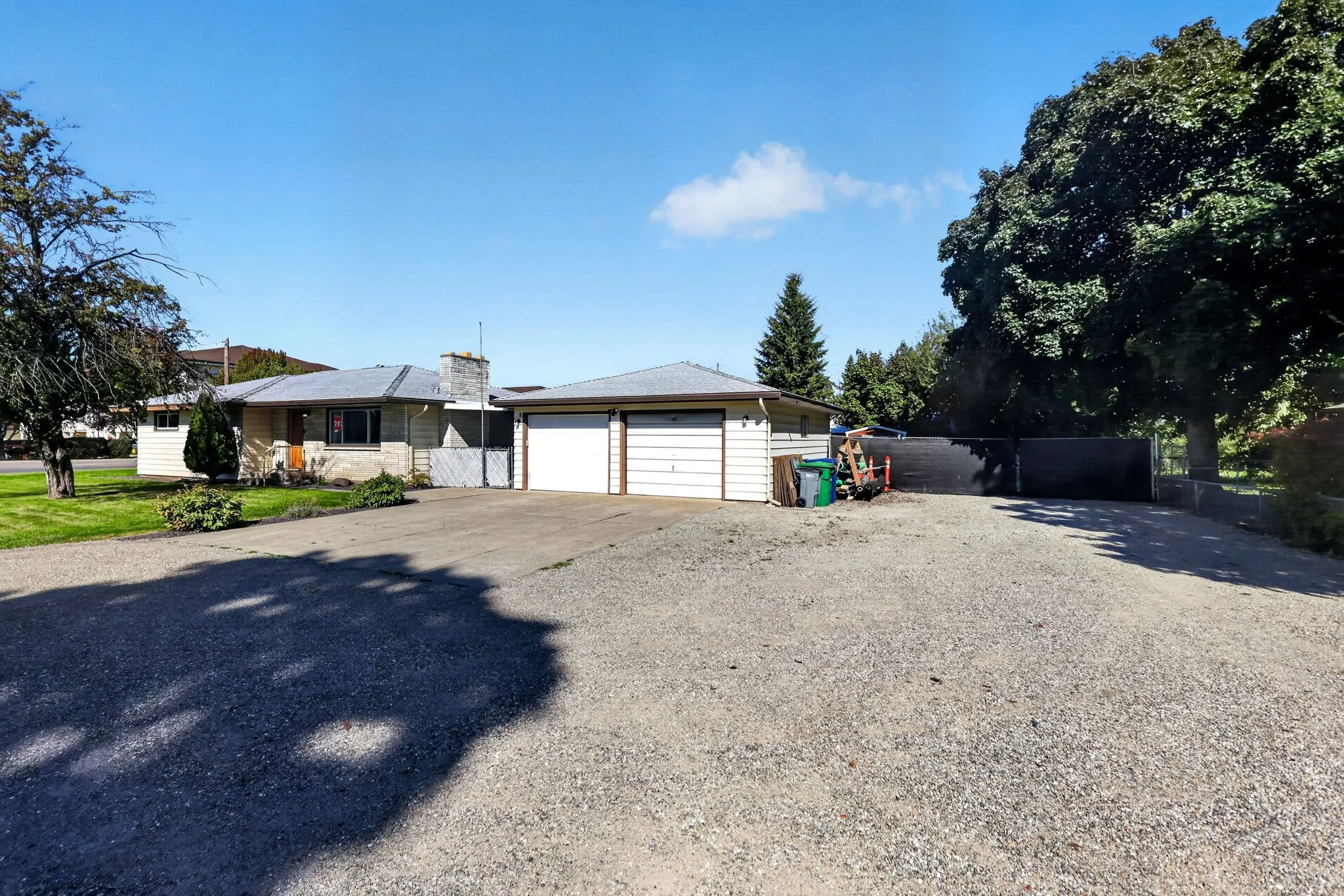 A suburban house with a dual garage, a driveway, trees, and a clear blue sky.
