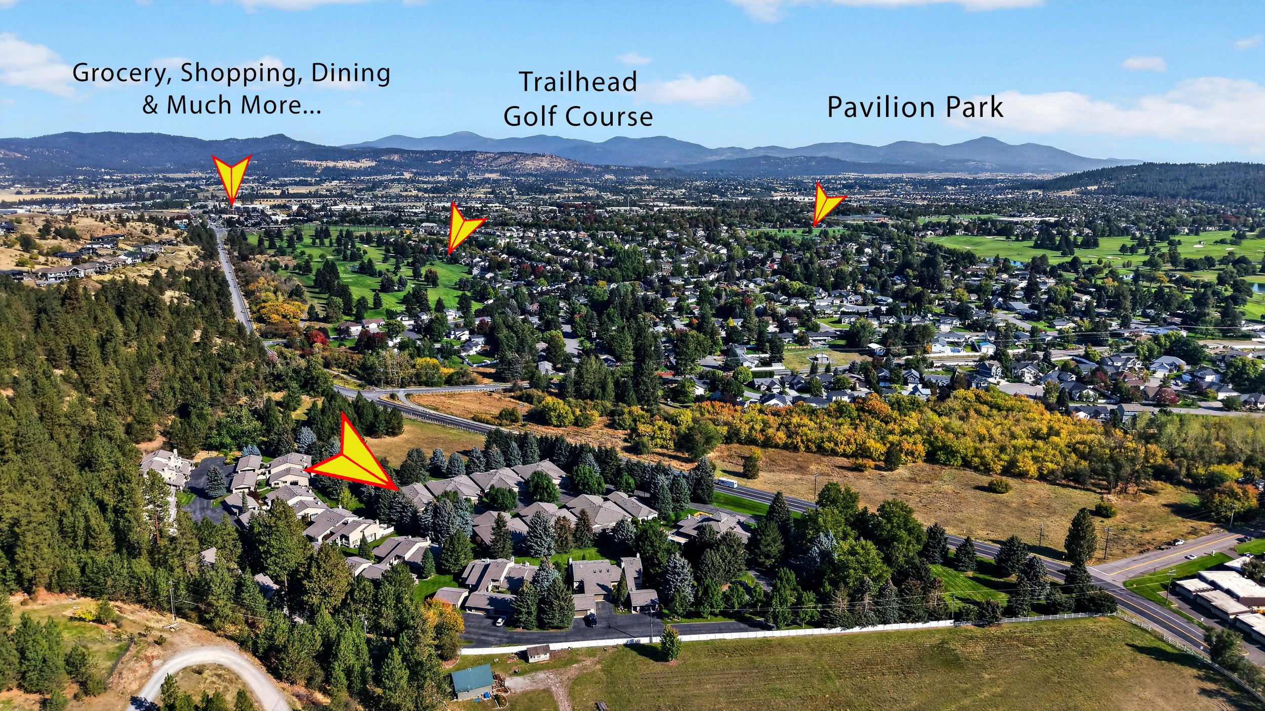 Aerial view of a suburban neighborhood with trees, houses, and roads, labeled with locations including grocery shopping, trailhead, golf course, and pavilion park, with distant mountains in the background.