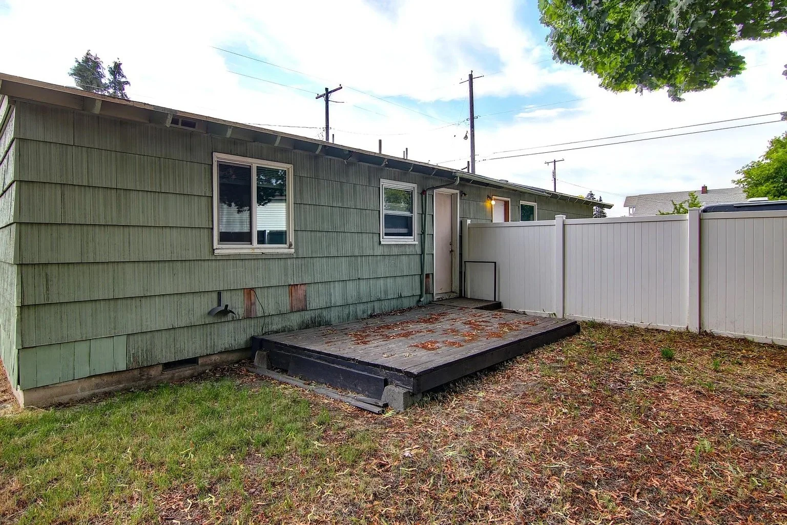Backyard with a small wooden deck, green house siding, and a white fence.
