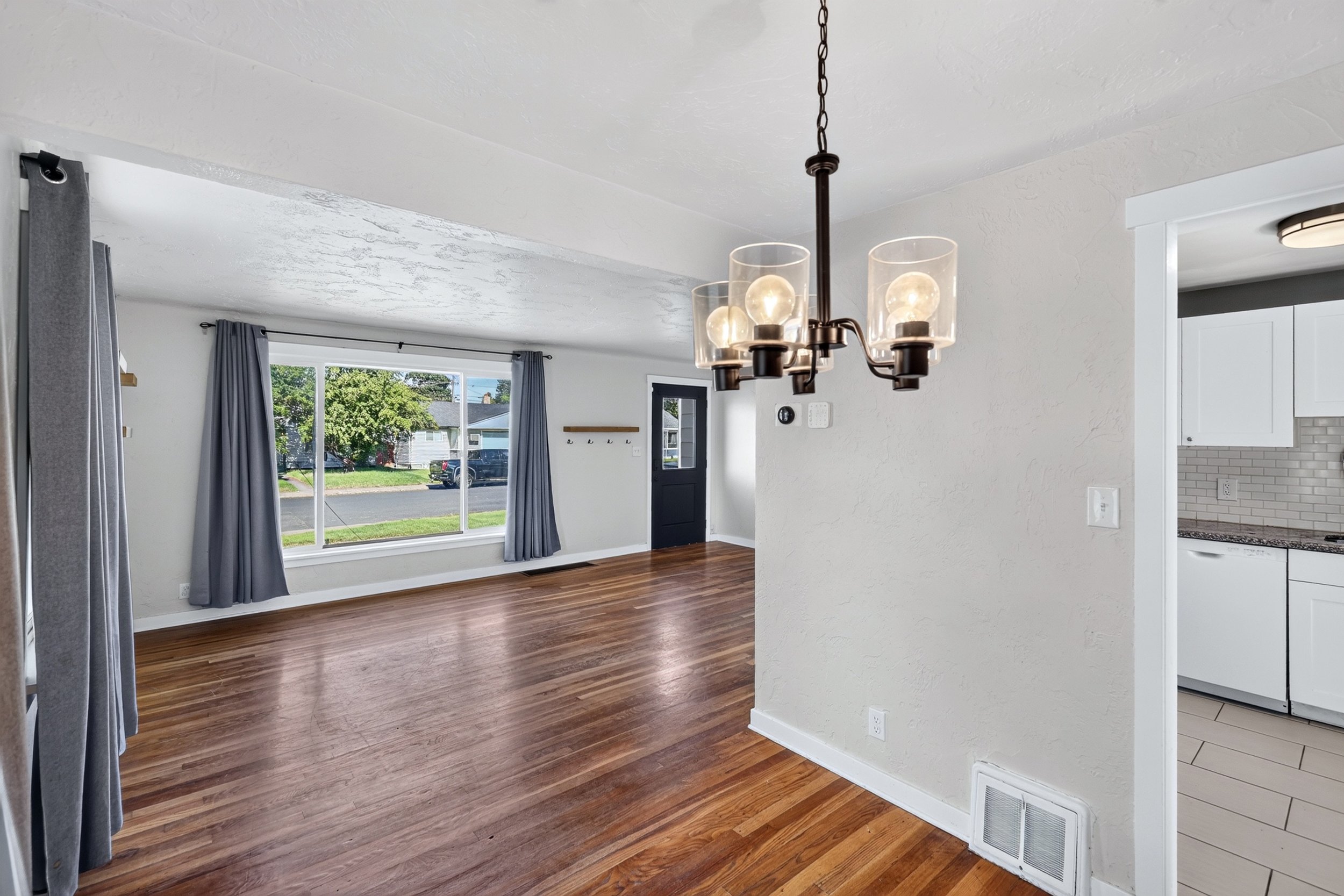 A bright living room with large window, hardwood floors, and a modern chandelier hanging from the ceiling.