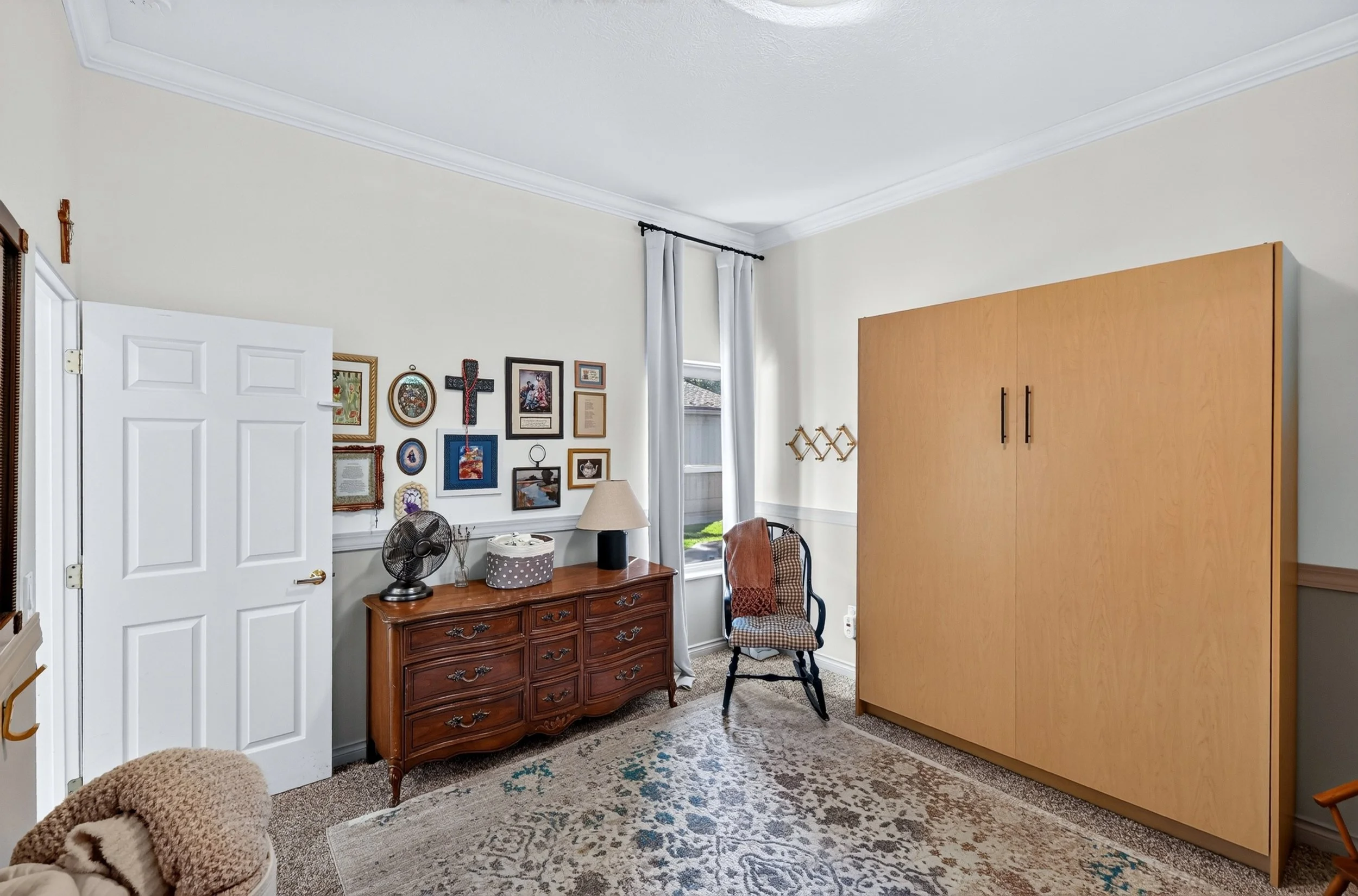 A living room with a gallery wall, wooden dresser, chairs, and a large wardrobe against the wall.
