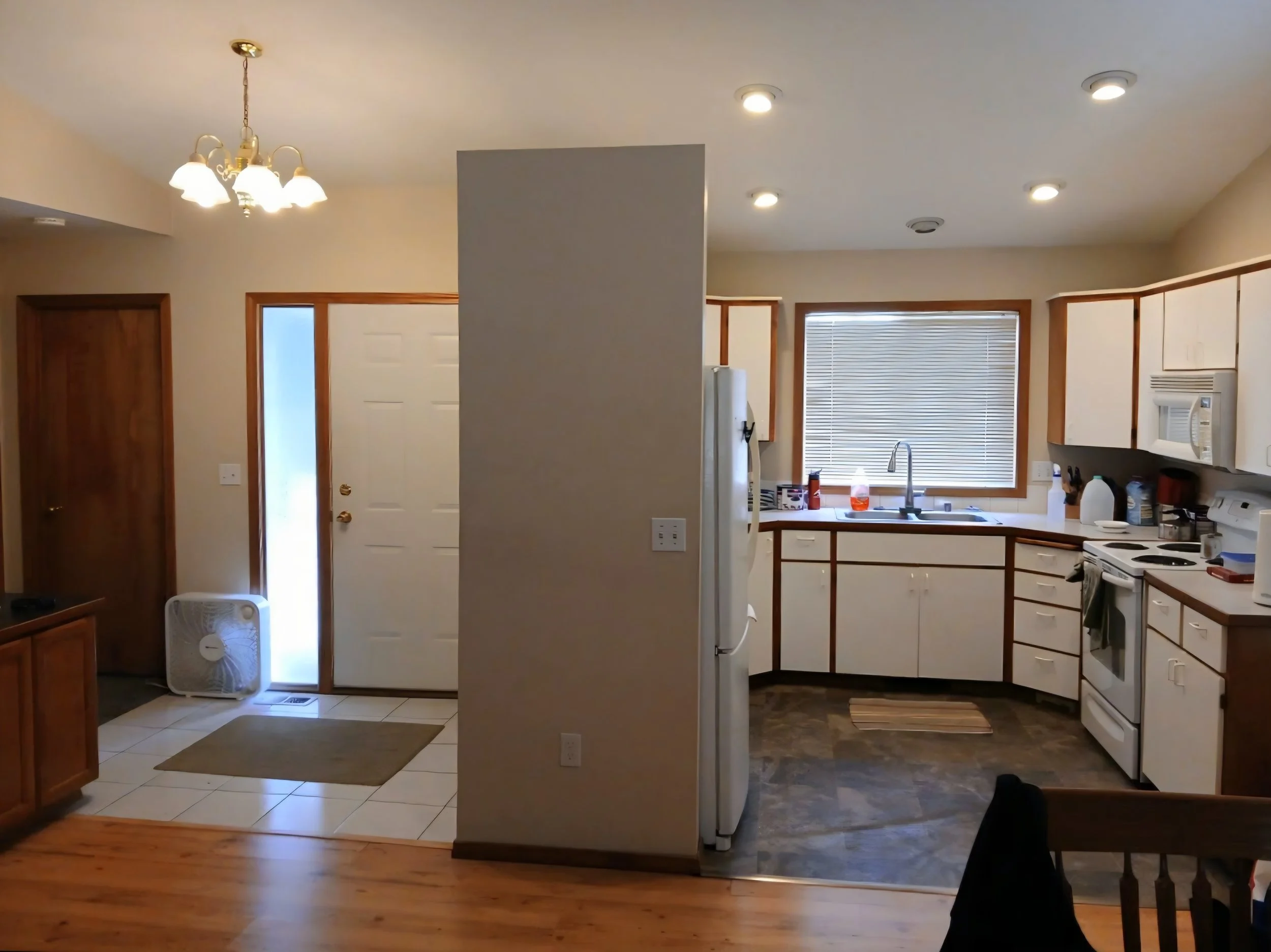 Interior view of a kitchen and entryway area with a white door, a breakfast nook with a window, and various appliances and furniture.