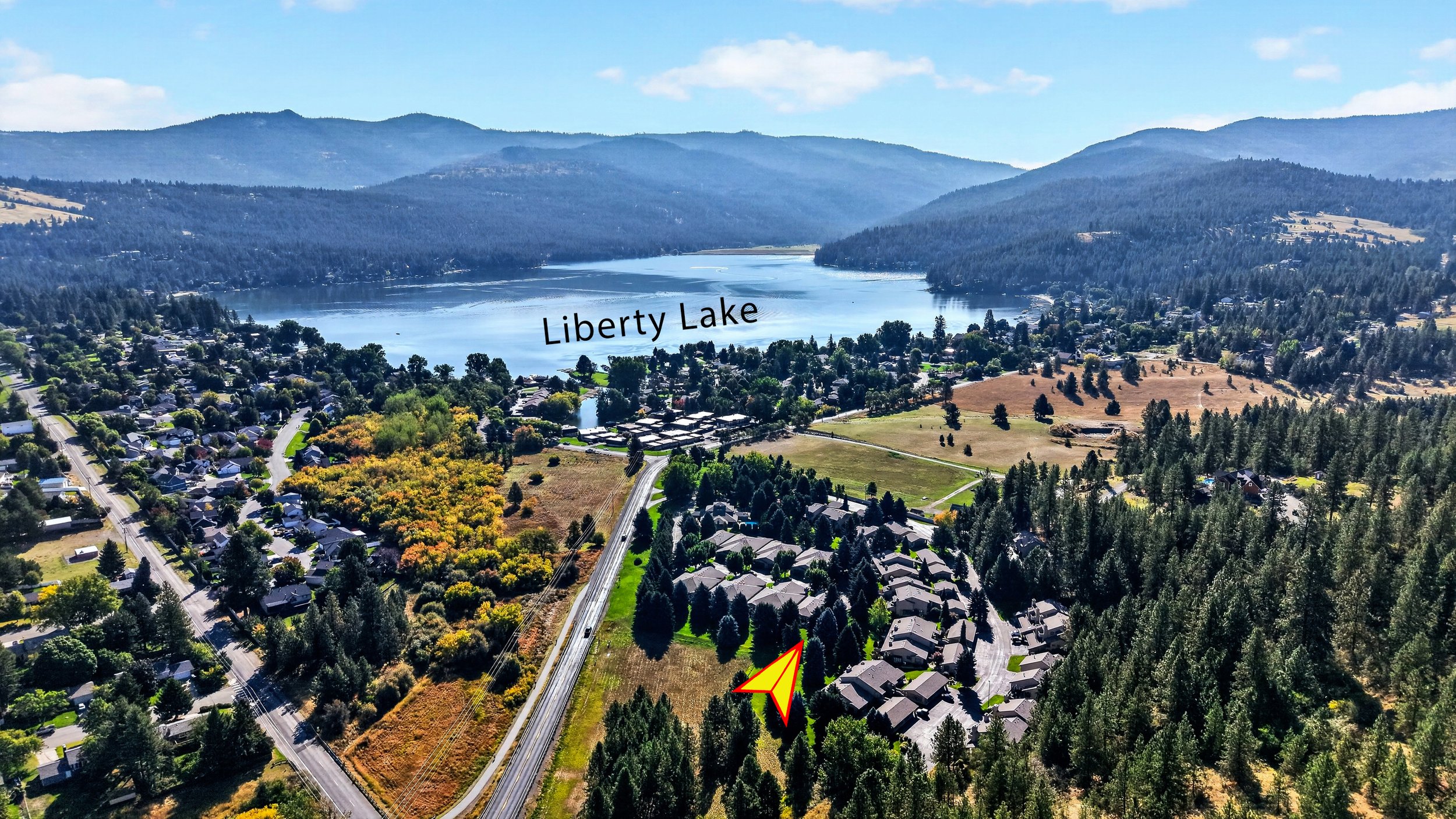 Aerial view of Liberty Lake with houses, a road, and a large body of water surrounded by forested mountains.