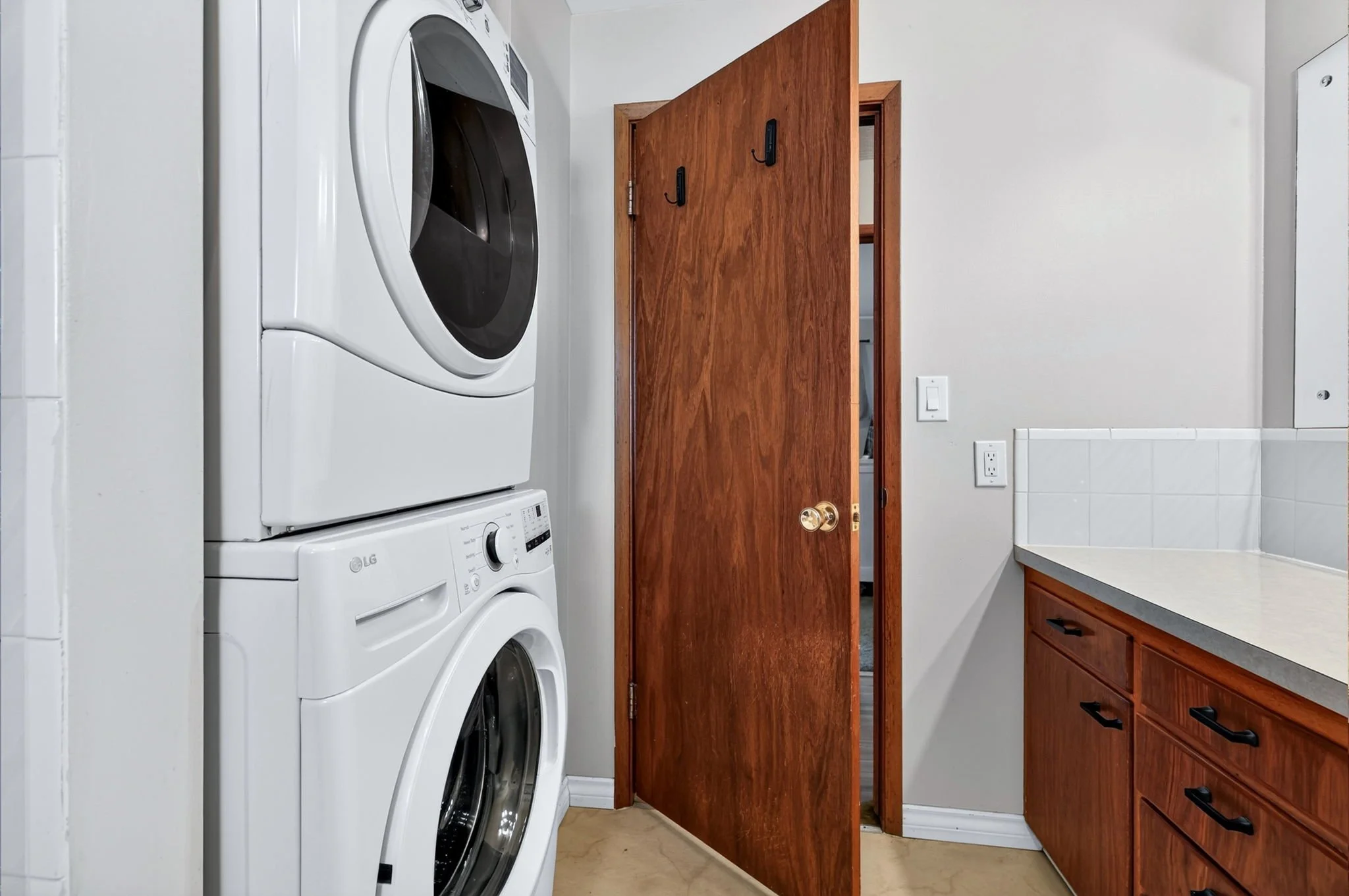 A laundry room with a stack of two white LG washing machines and a wooden cabinet with black handles.