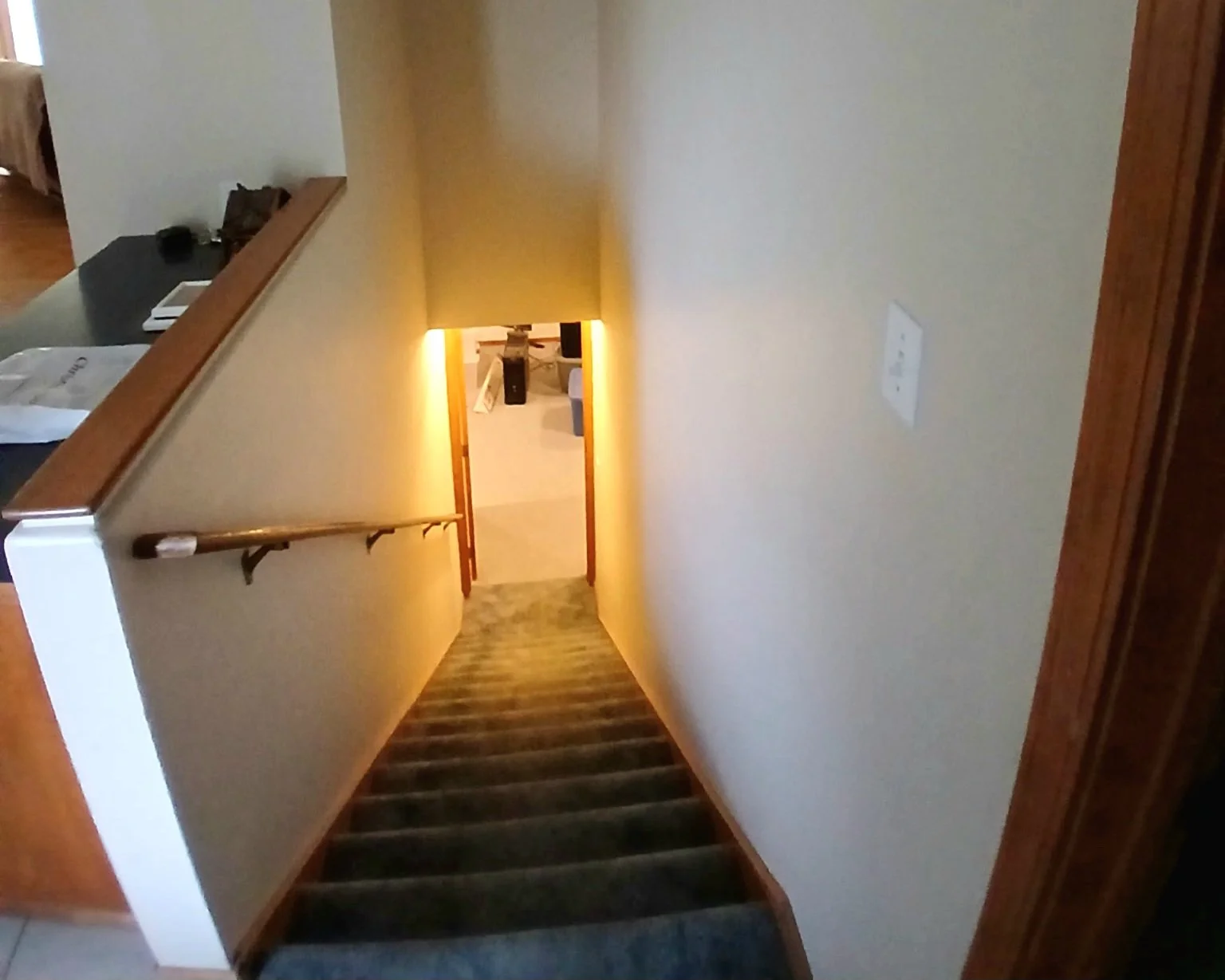 Staircase with wooden handrail leading down to a doorway with warm lighting in a residential home.