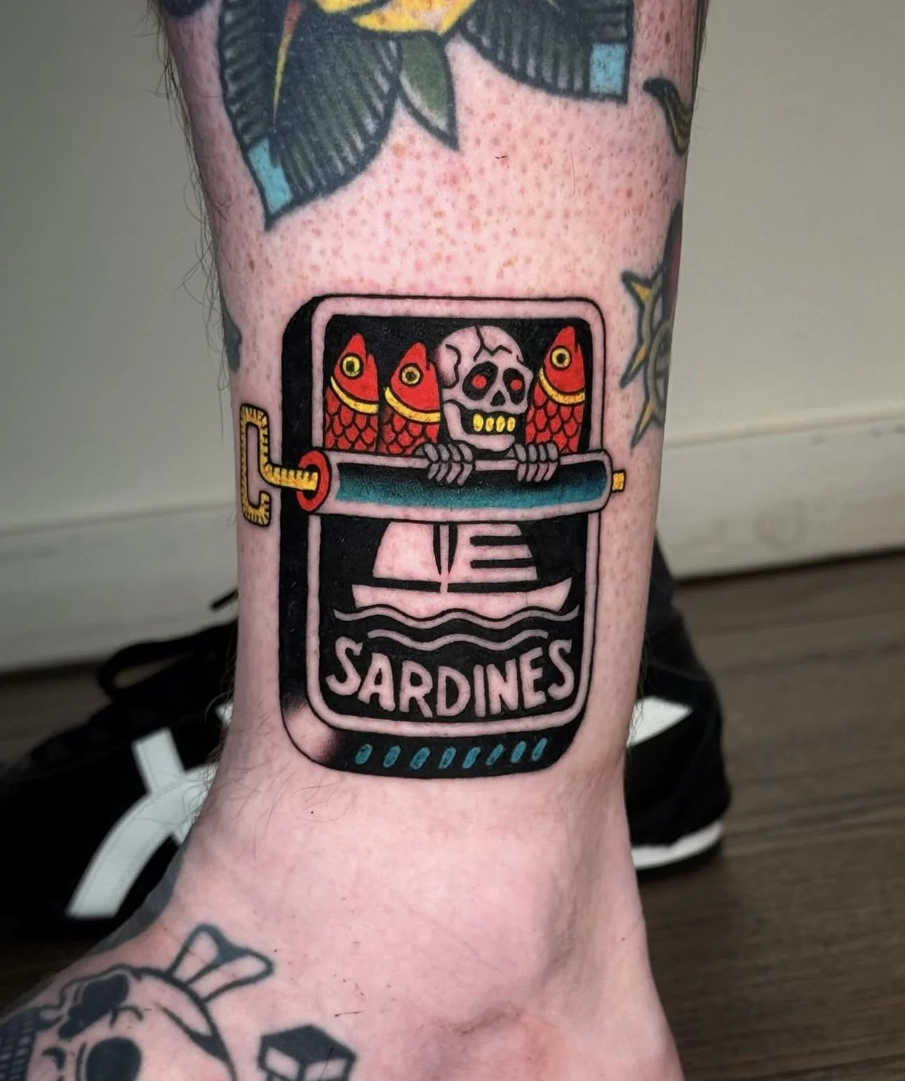 Tattoo of a sardine can with a skull and fish inside, labeled 'SARDINES'.