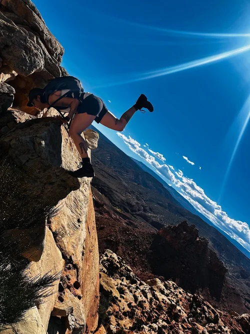 Cynthia scrambling down a sandstone ledge above a canyon