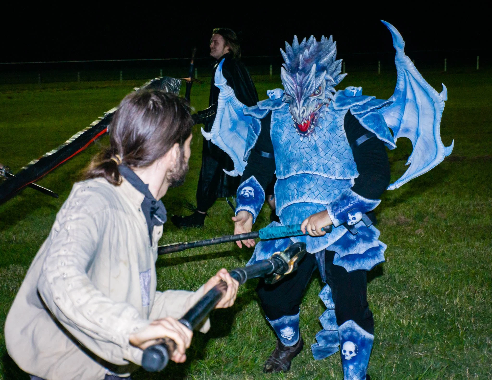 Two people in cosplay costumes facing each other, one dressed as a blue dragon and the other as a human with a microphone, outdoors at night.