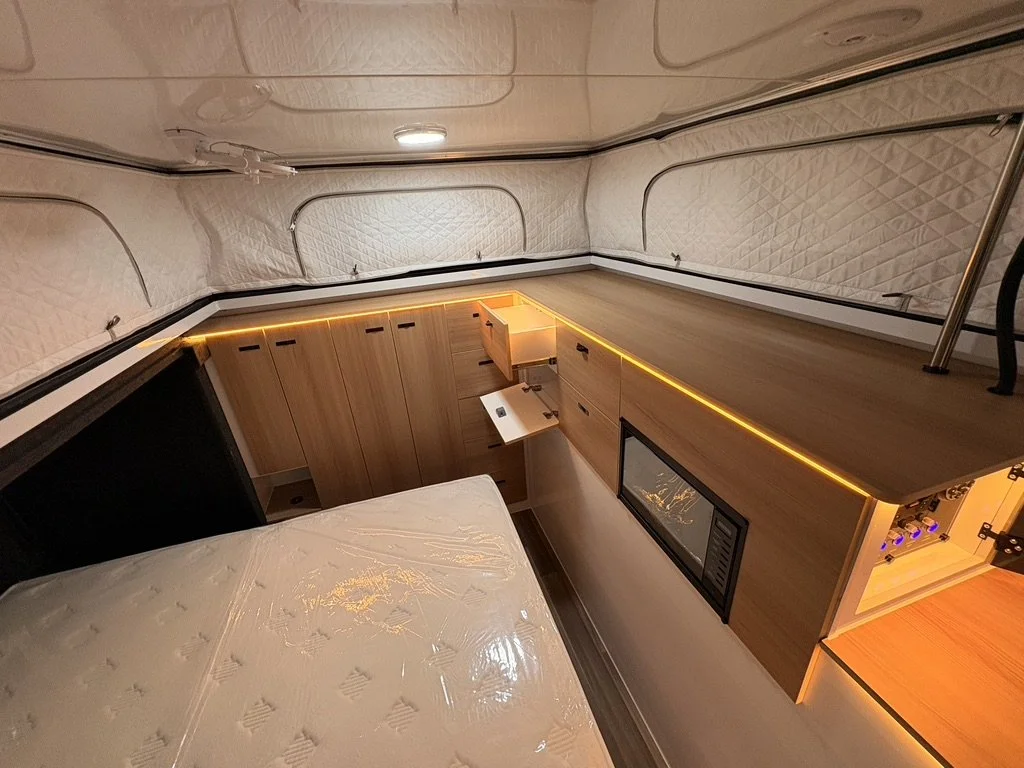 Interior of a compact living space with a bed, wooden cabinetry, a built-in microwave, and ambient LED lighting.