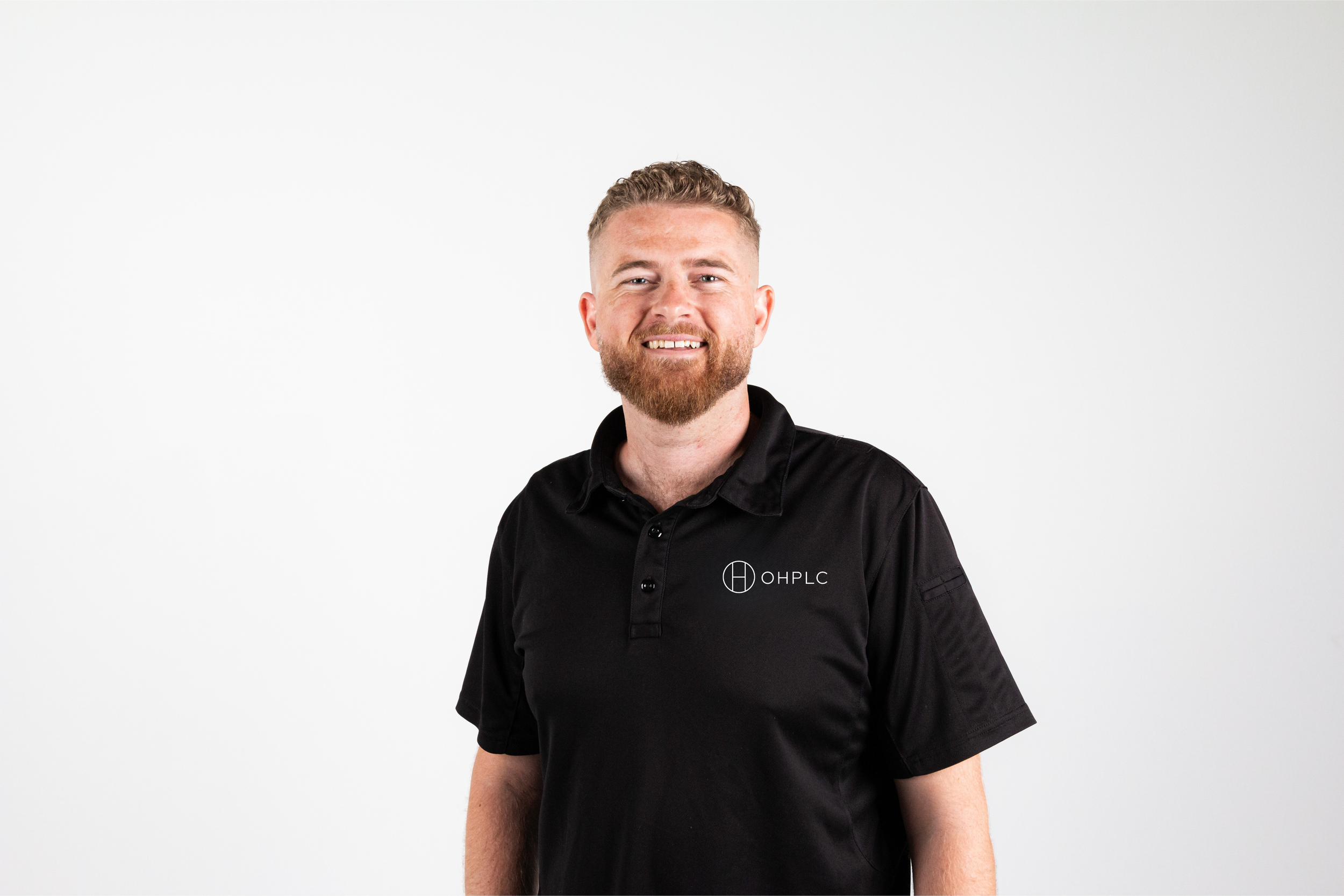 A smiling man with a beard wearing a black polo shirt with the 'OHPLC' logo stands against a plain white background.