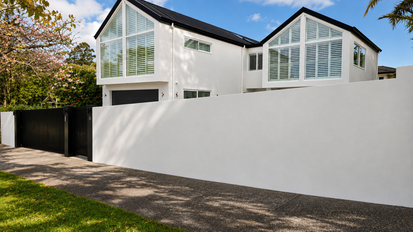Contemporary Auckland home with a white rendered boundary wall, black aluminium sliding gate, architectural lighting and modern street frontage.