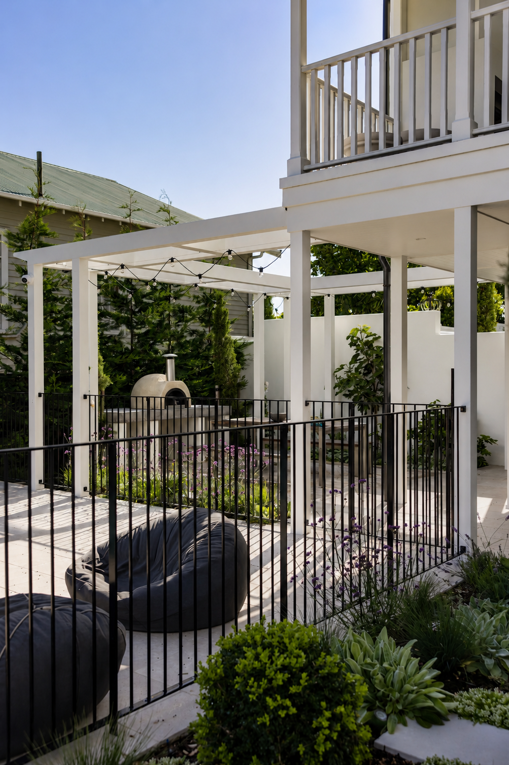 Modern black steel pool fencing surrounding an outdoor entertaining area with pergola, pizza oven, landscaped gardens, and premium residential backyard in Auckland, New Zealand.