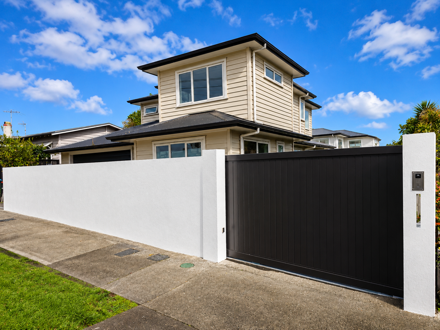 Modern black aluminium sliding gate with rendered white boundary wall and integrated keypad entry at a contemporary Auckland home.